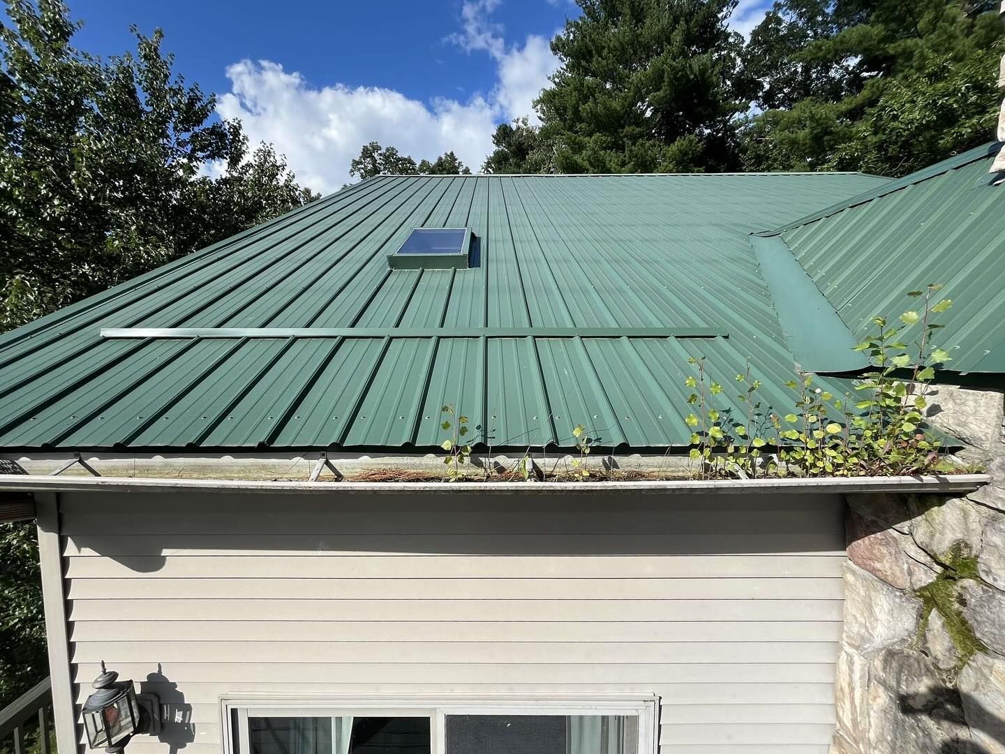 Green metal roof over white house with skylight under a blue sky.