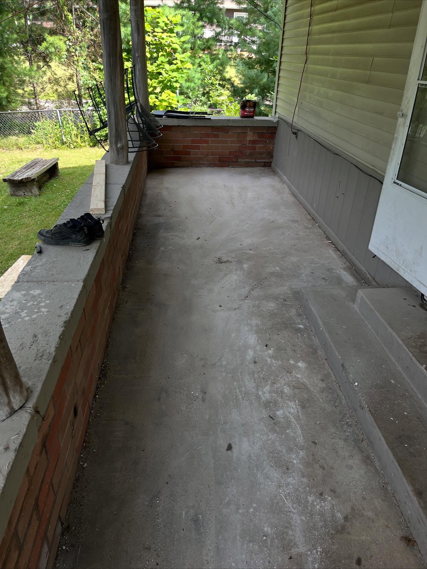 Narrow concrete porch with brick half-walls, white siding, and a green yard beyond.