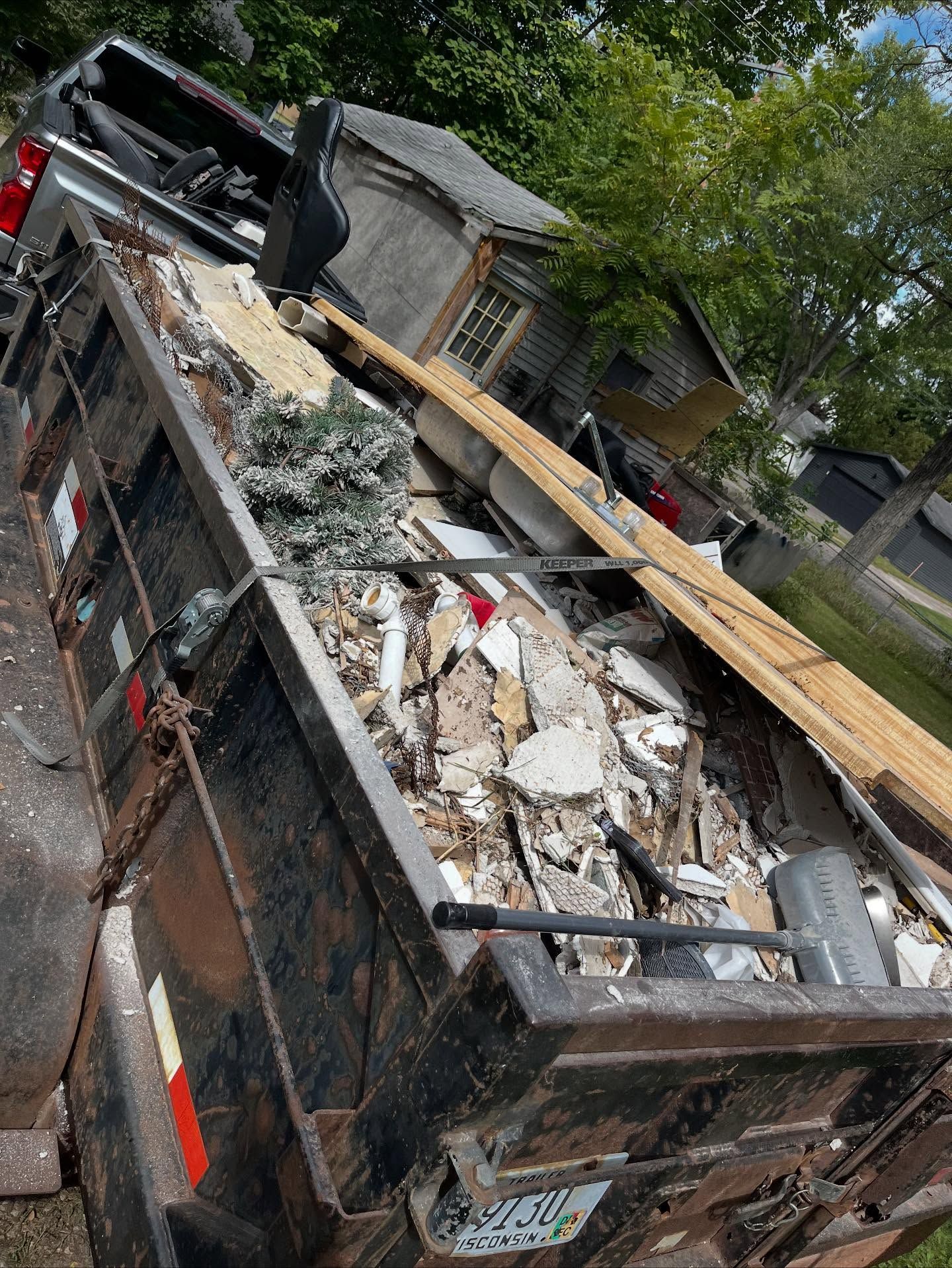 Overturned dump truck loaded with rubble and debris on a residential street beside houses and trees