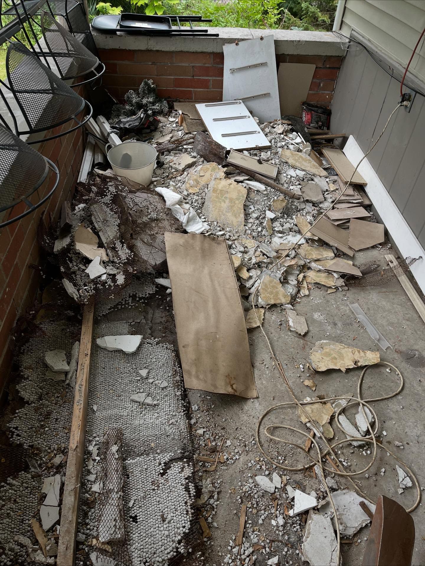Damaged patio with broken concrete, scattered debris, and a boarded opening near the wall