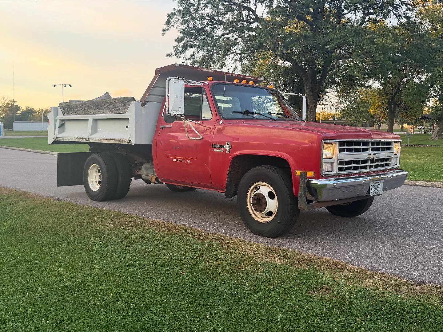 Red flatbed work truck parked on a road beside grass and trees at sunset