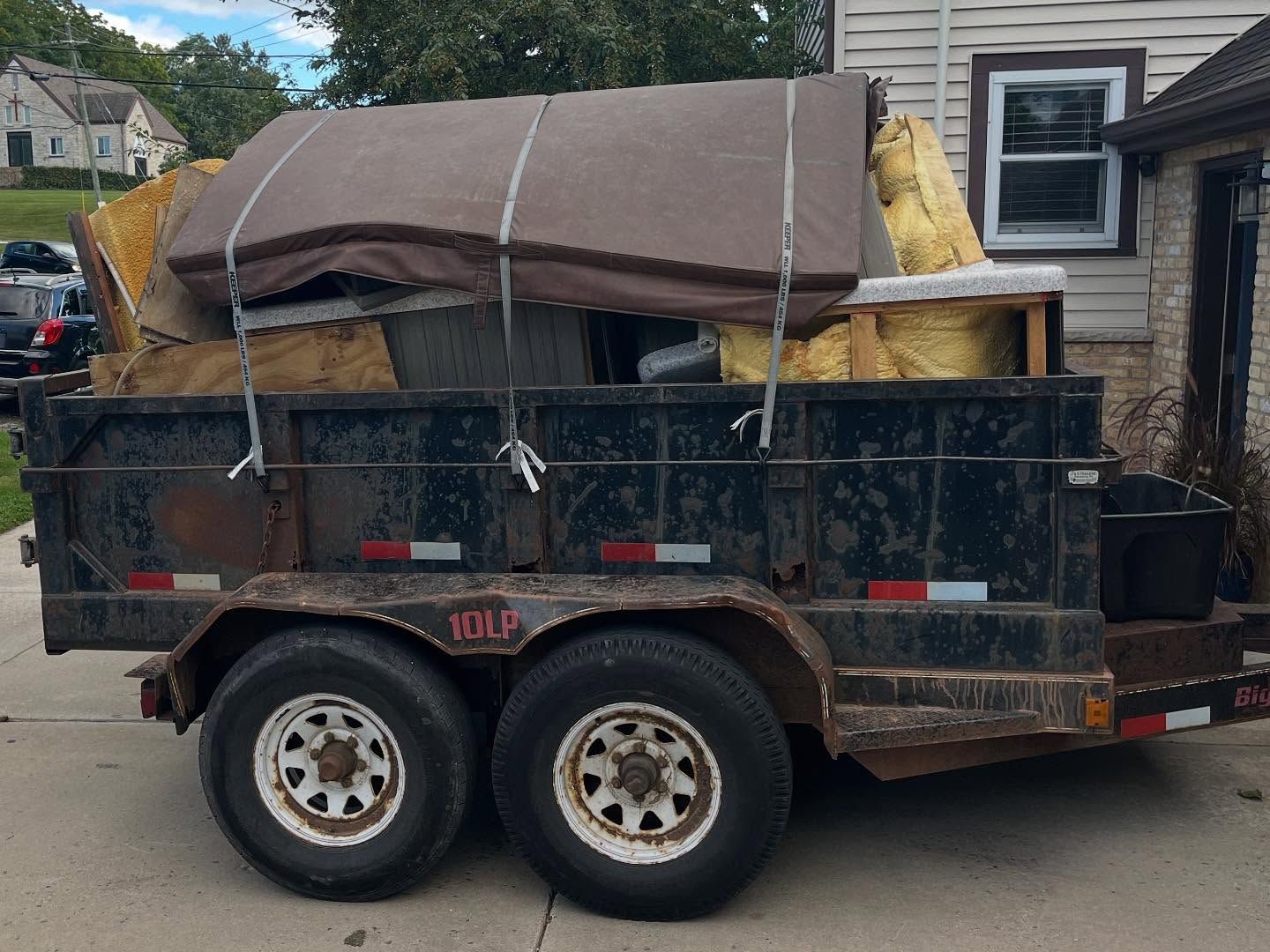 Dump trailer loaded with furniture and yellow insulation, parked on a residential street