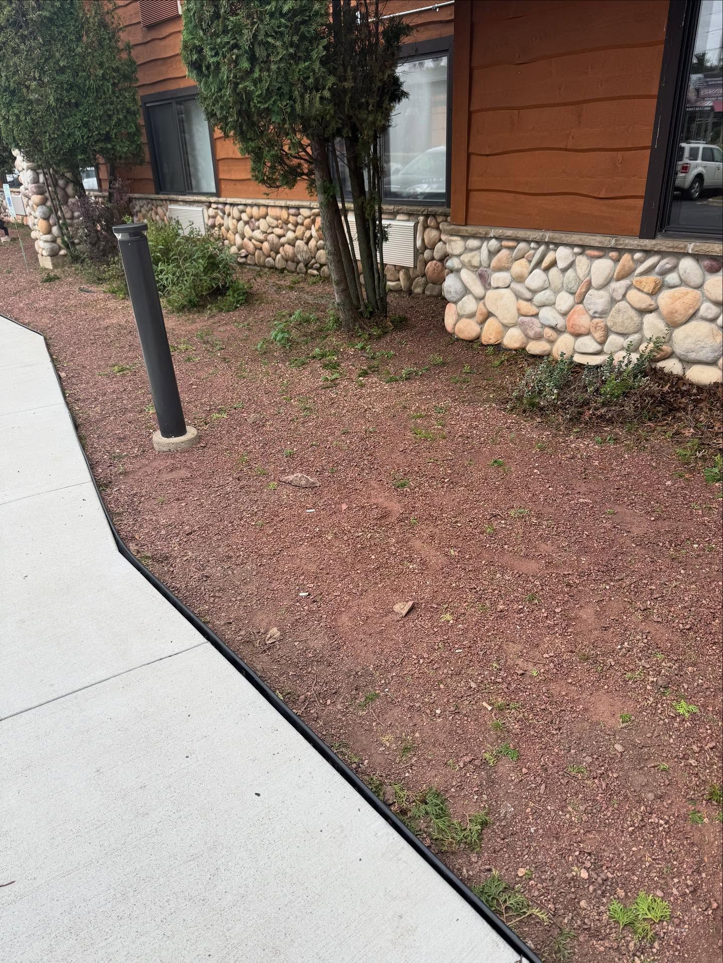 Sidewalk beside a gravel landscaping bed, black bollard, and building with stone and wood siding