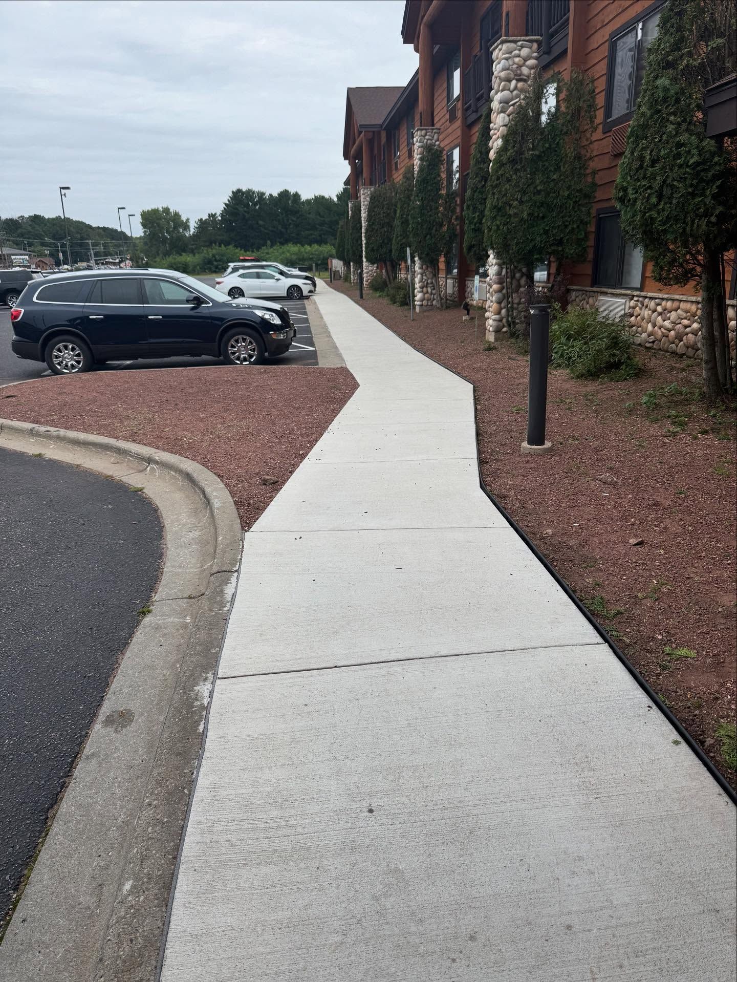Curved sidewalk beside parked cars and brick building with black lampposts and red mulch
