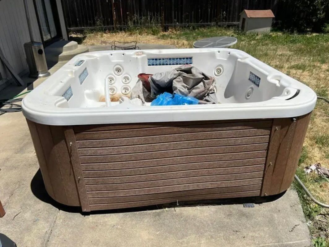 Outdoor hot tub with wicker-style siding, filled with assorted items in a backyard.