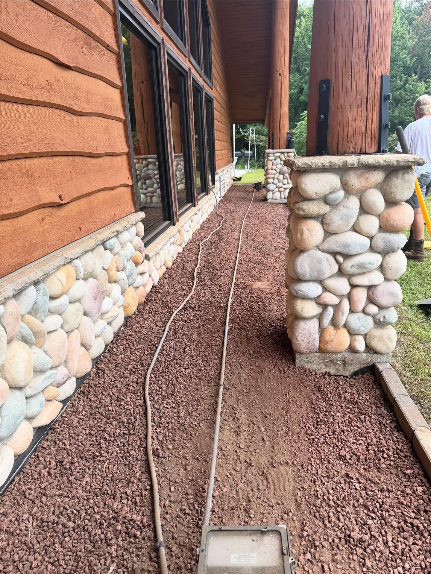 Stone walkway along a rustic building with pebbles and gravel landscaping, leading past a porch column