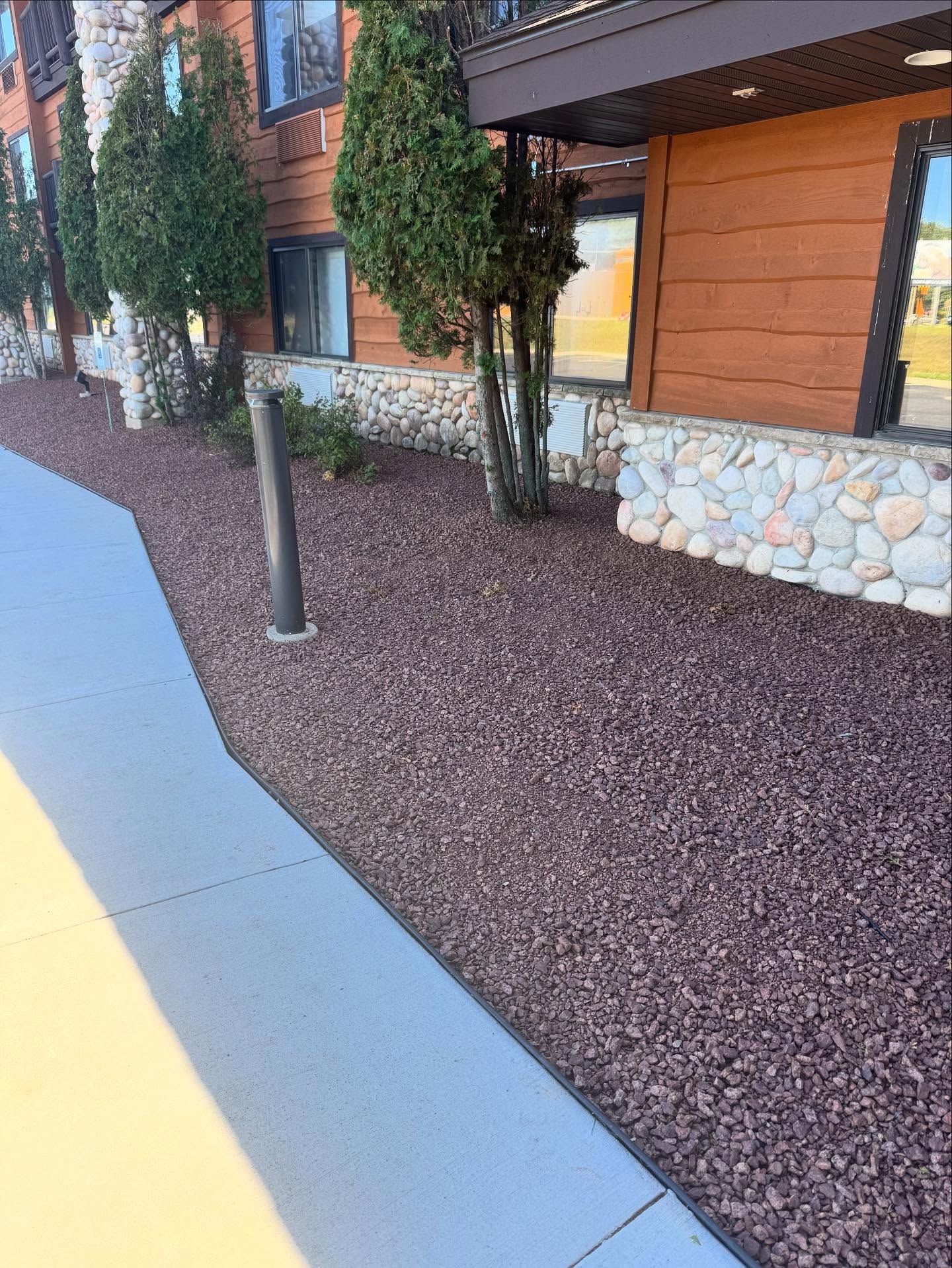 Apartment building walkway with tan sidewalk, brown landscaping, and stone-accented exterior walls