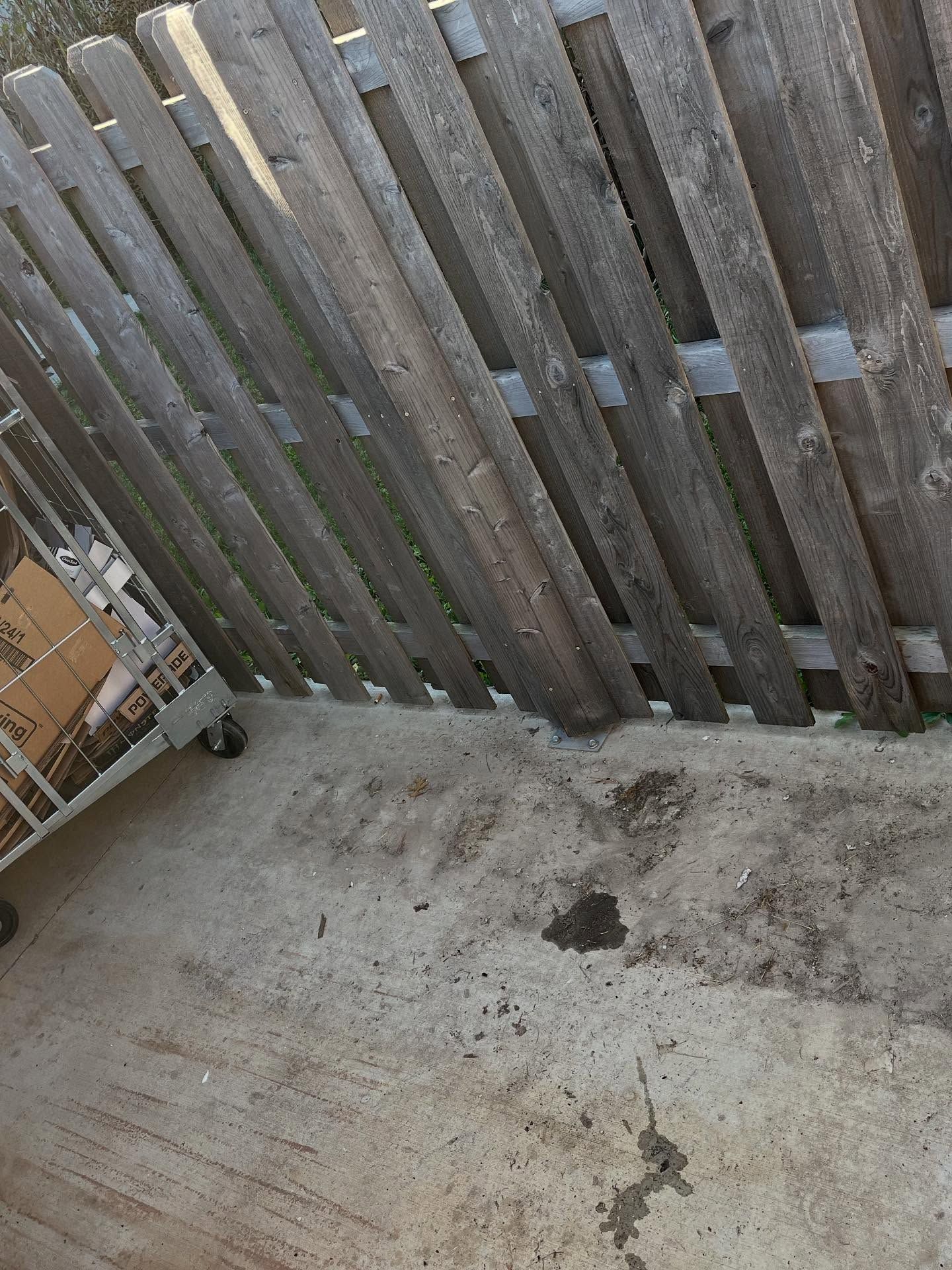 Weathered wooden fence beside a stained concrete patio and scattered debris