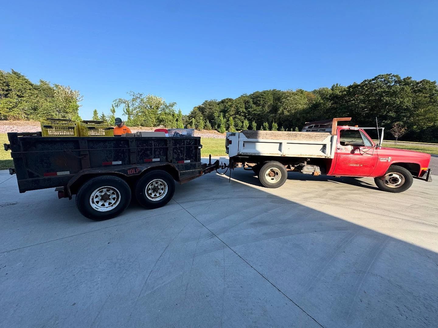 Red pickup truck towing a black dump trailer in a sunny parking lot