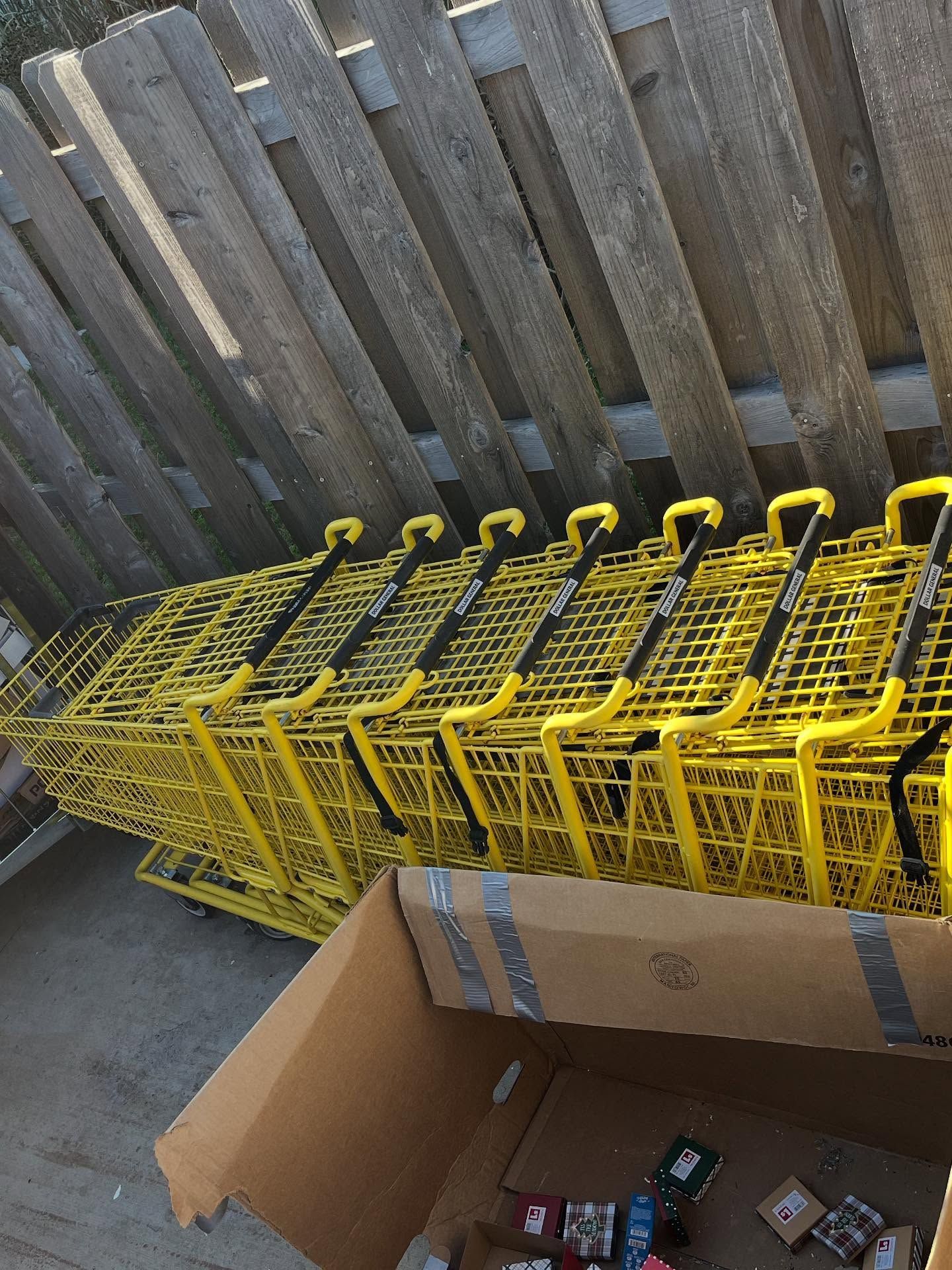 Stacked yellow toy shopping carts beside an open cardboard box on a concrete floor.