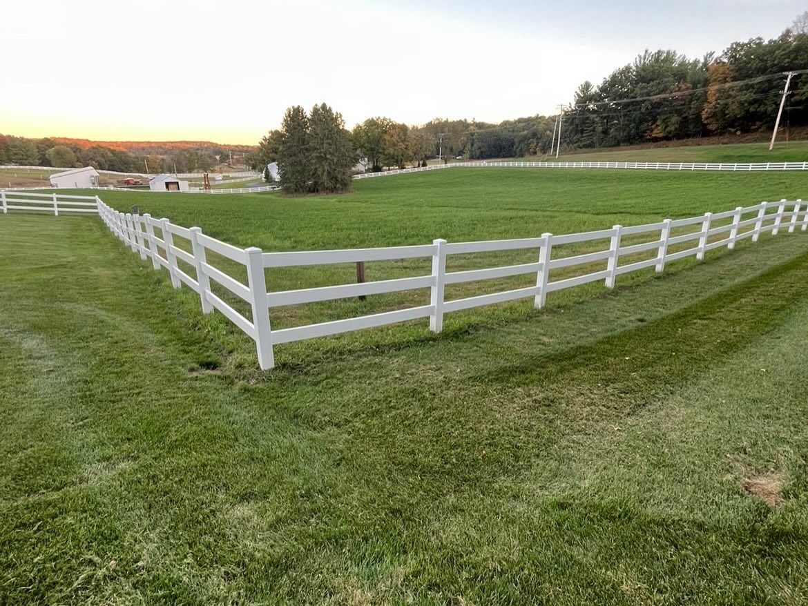 White wooden fence encloses a grassy field at sunset with trees in the background.