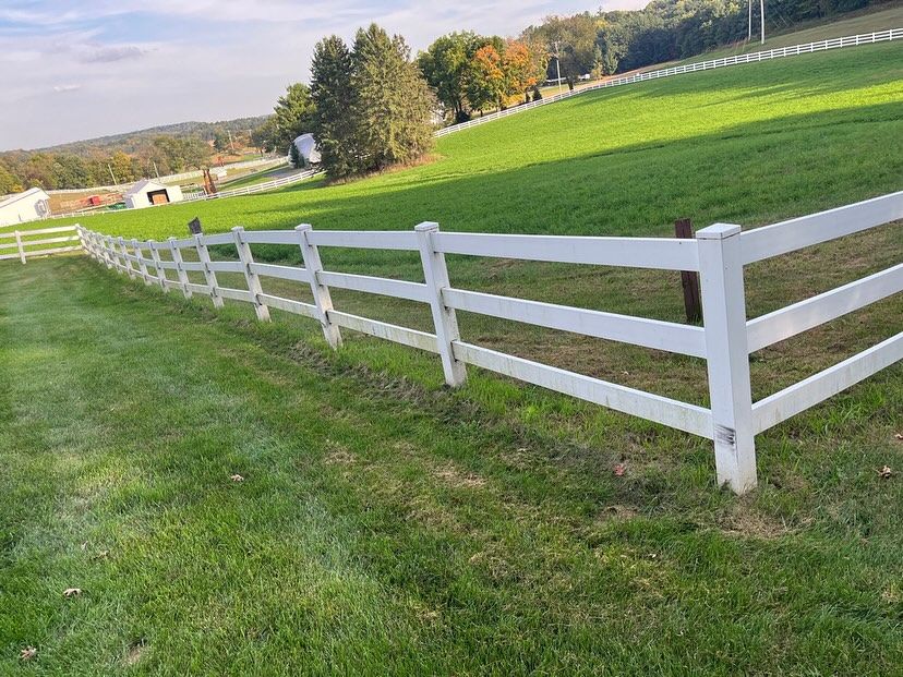 White rail fence beside a green grassy field under a clear sky in a rural landscape