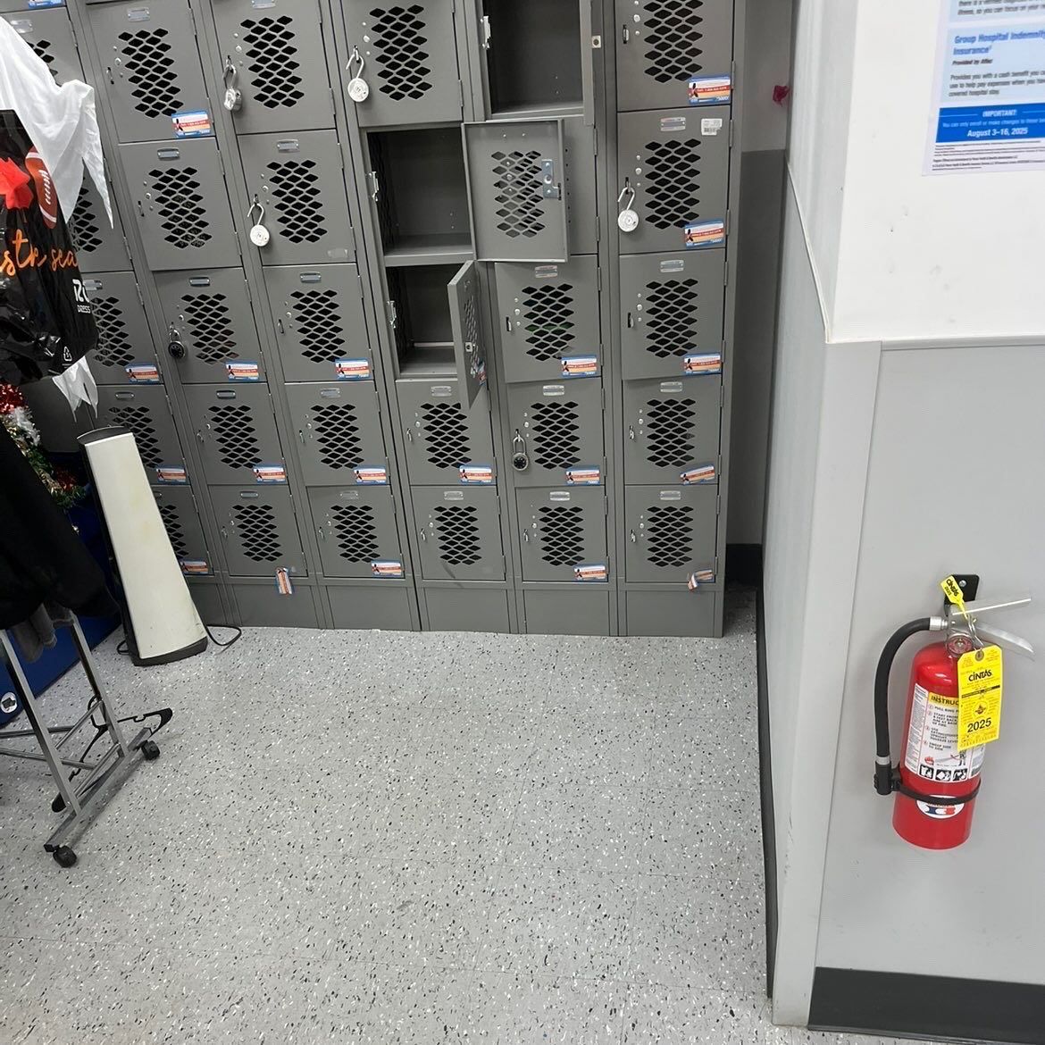 Gray lockers in a store back room, with a red fire extinguisher on the right wall.