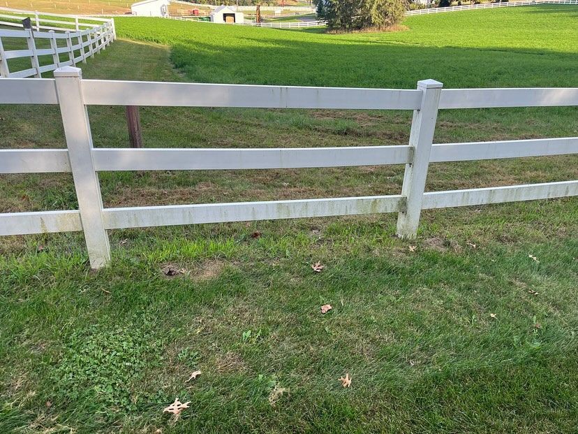 White wooden fence along a grassy path in a park, with a curving fence in the background.