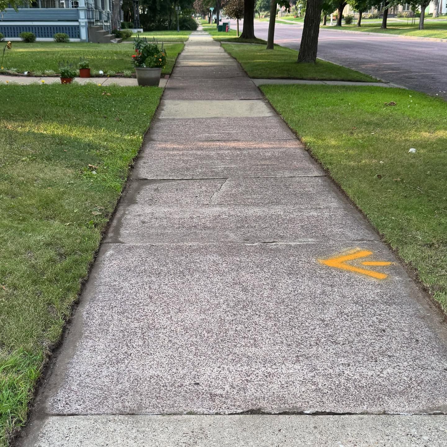 Sidewalk beside a grassy lawn and road, with a yellow arrow marking on the pavement.