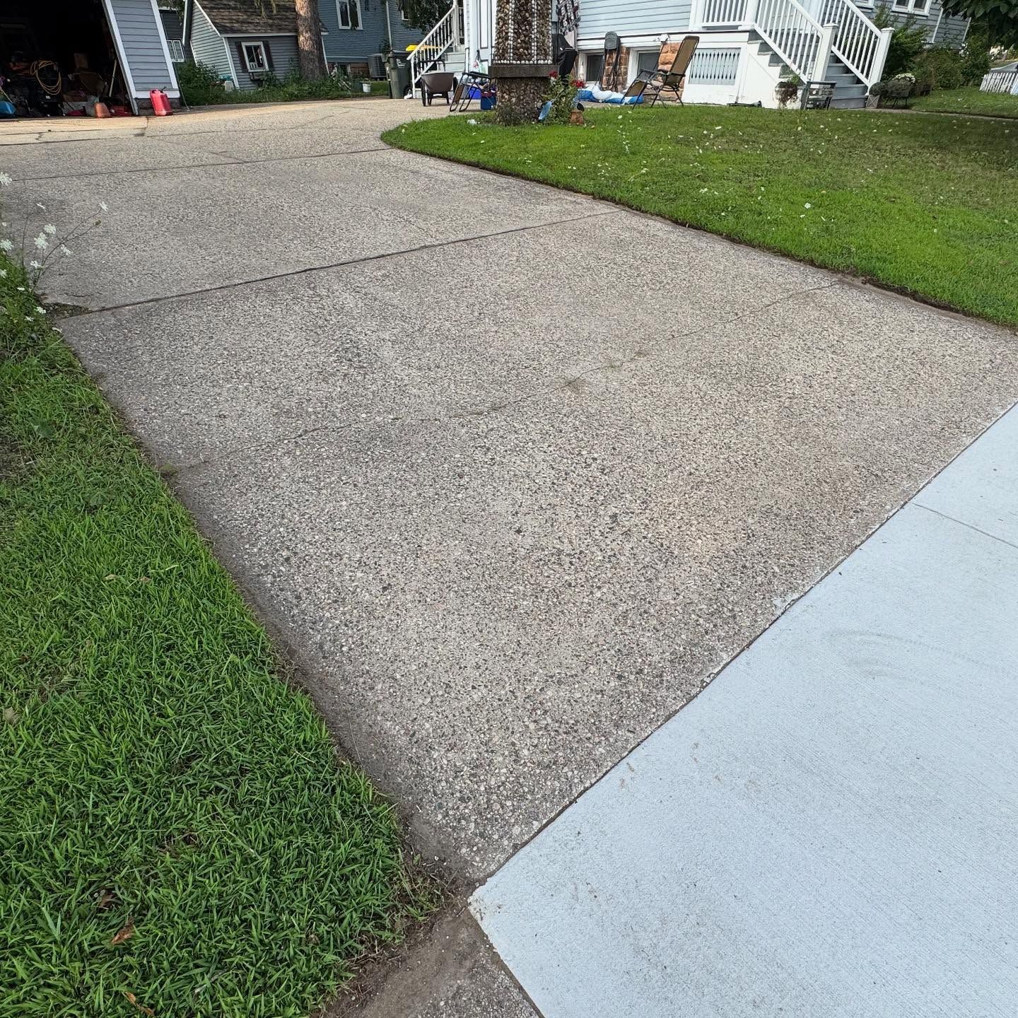 Cracked concrete driveway beside green grass and a light blue sidewalk, leading to a house