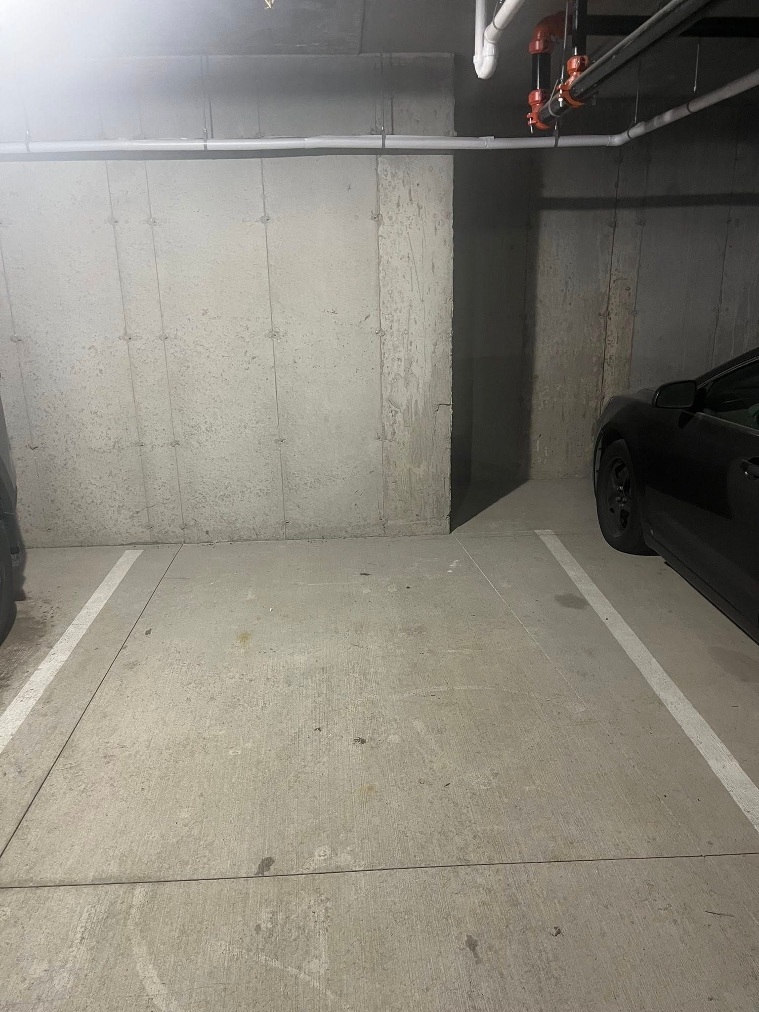 Empty concrete parking garage space with marked lines and a dark car on the right