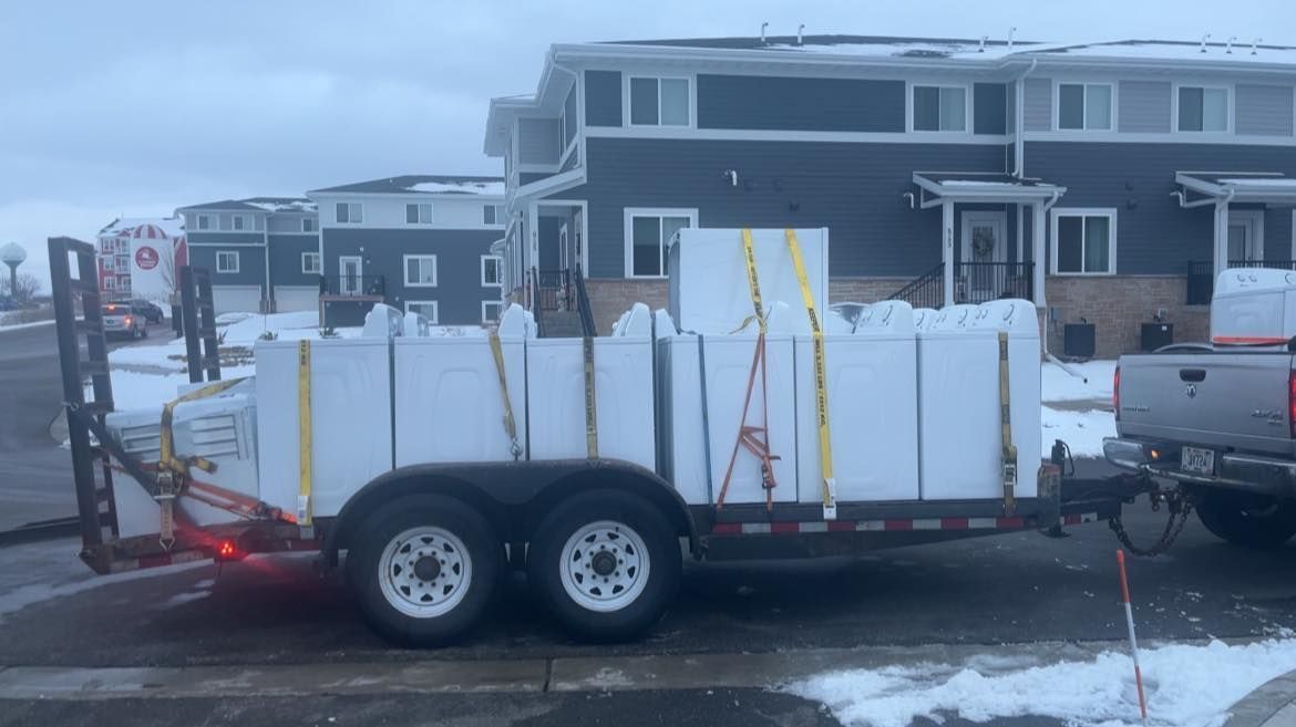 Trailer loaded with white boxes parked in snowy lot beside gray apartment buildings