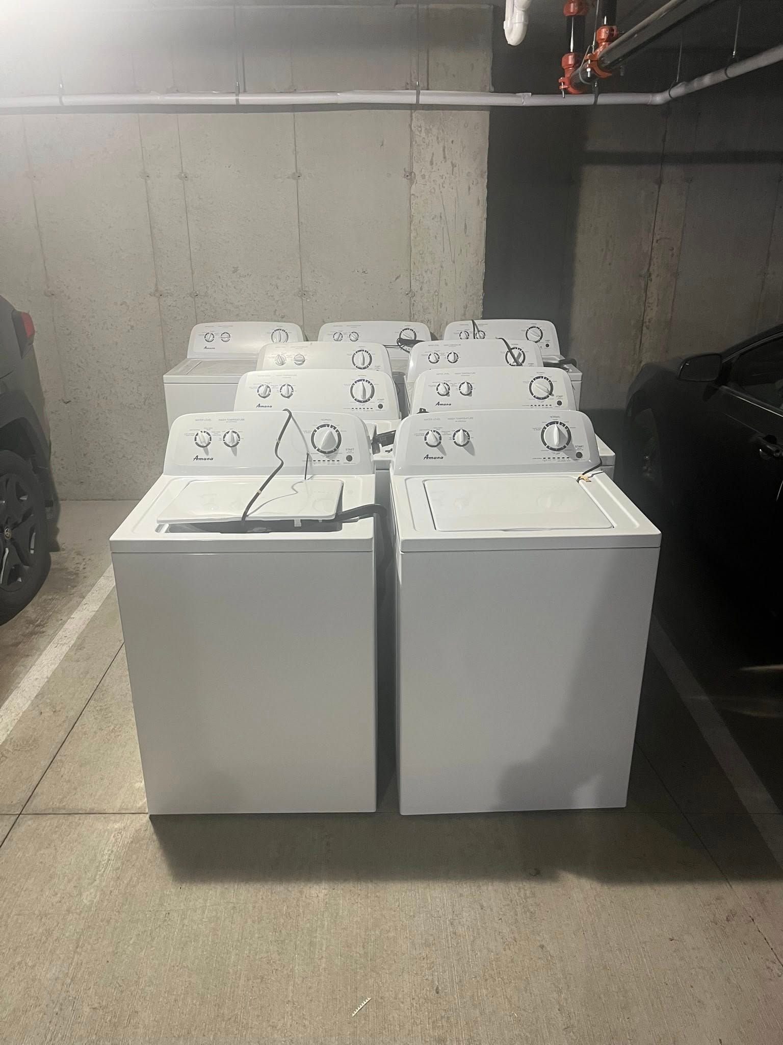 Four white top-loading washing machines lined up in a concrete basement laundry room.