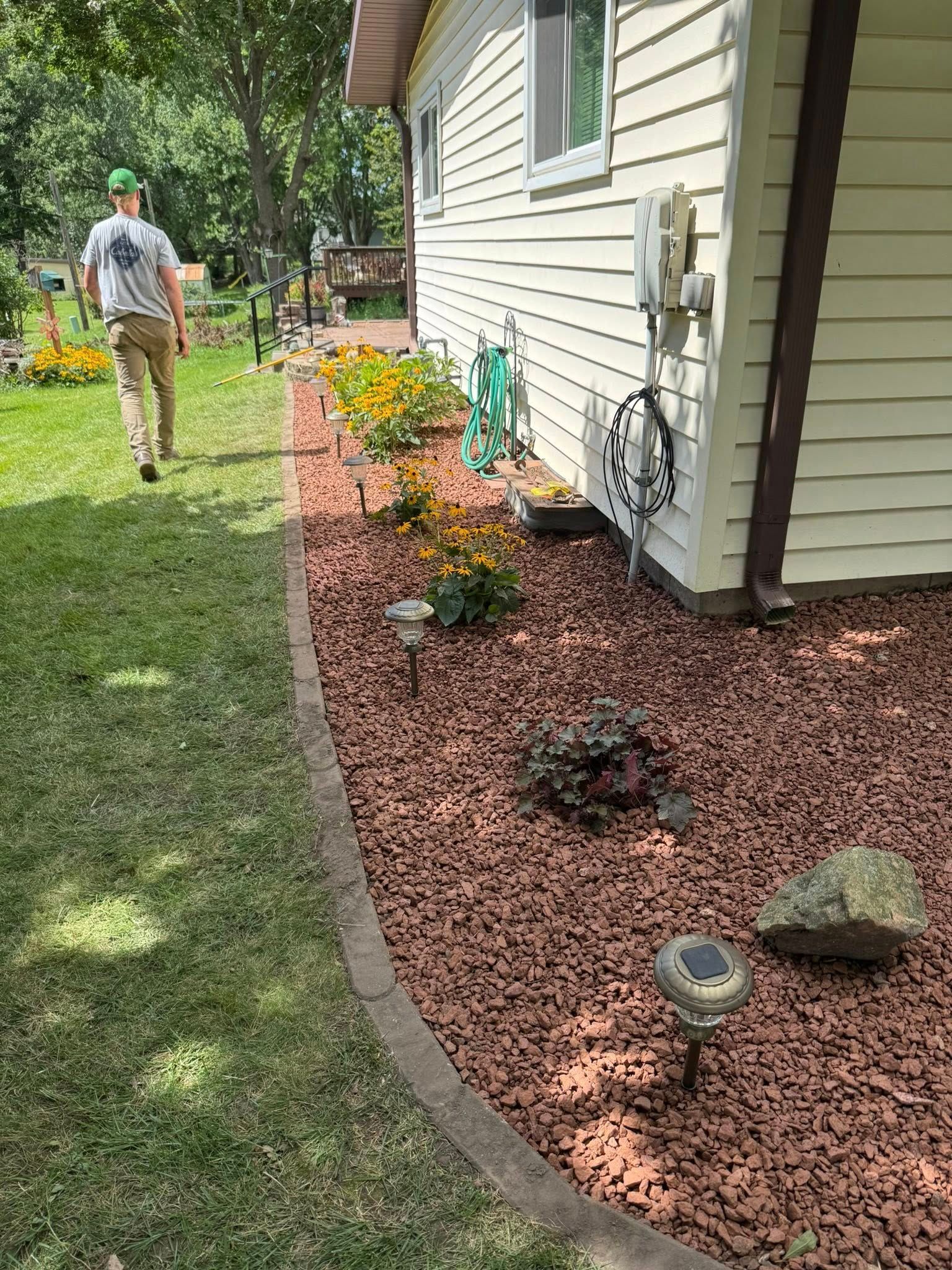 Man walking beside a house with a red mulch garden bed and green lawn