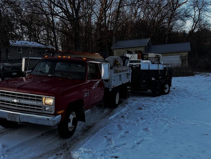 Red tow truck pulling a black truck on a snowy driveway at dusk