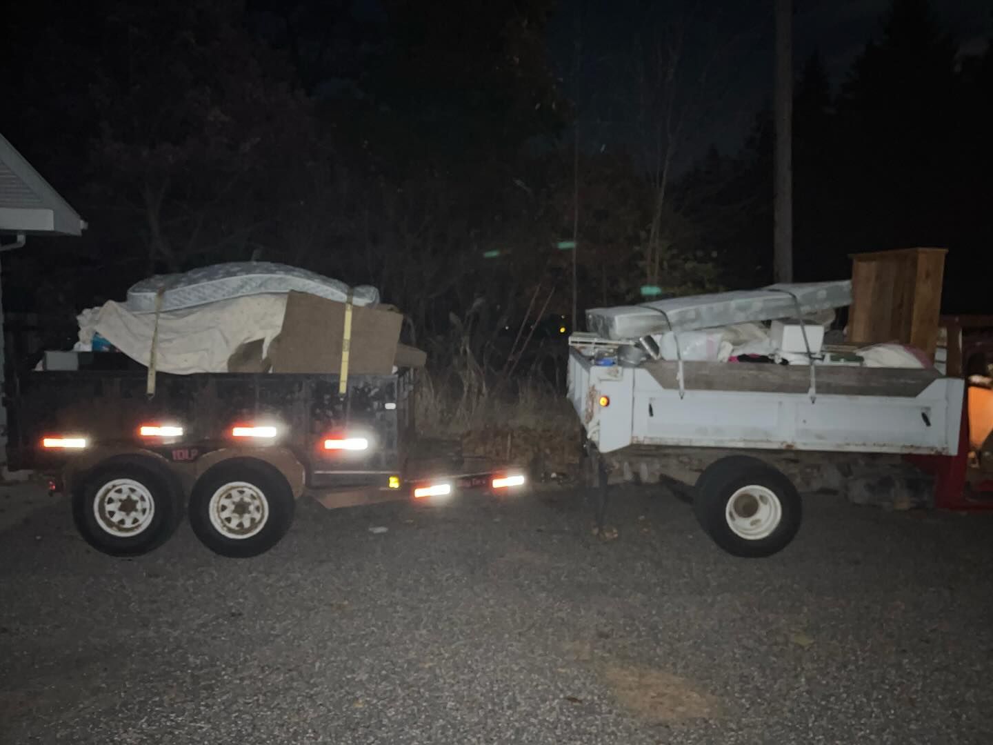 Two small utility trailers loaded with covered cargo parked on a dark roadside at night