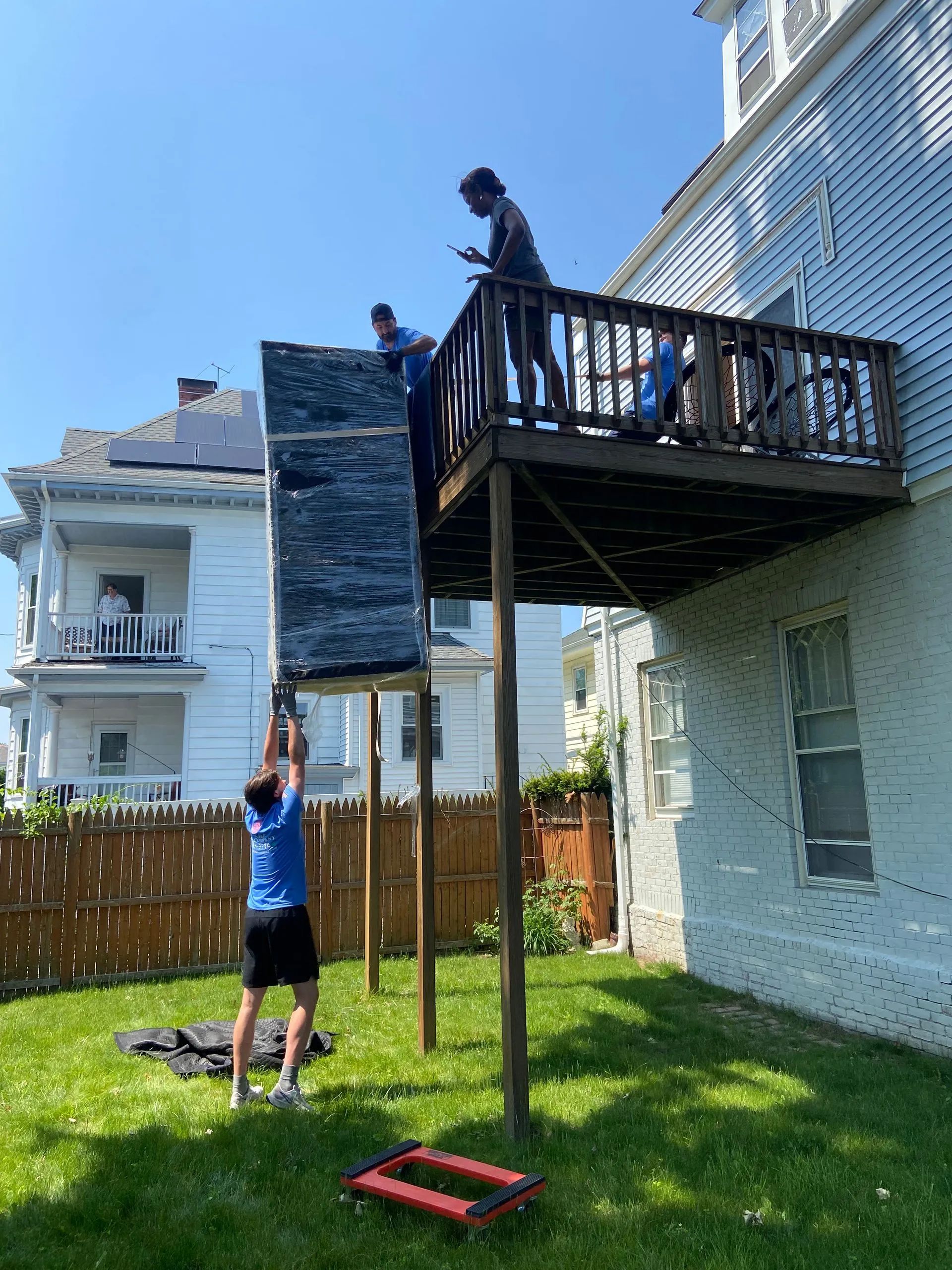 Two people on an elevated deck, one helping another climb up from the lawn in a backyard.