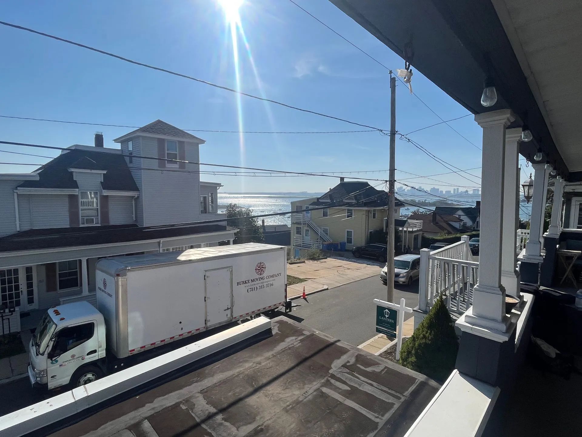 Bright sunny street with a white box truck parked beside houses, seen from a porch.