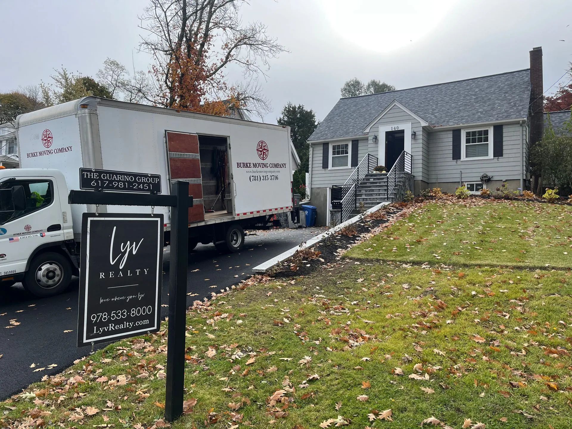 Moving truck parked in front of a gray house. Sign: