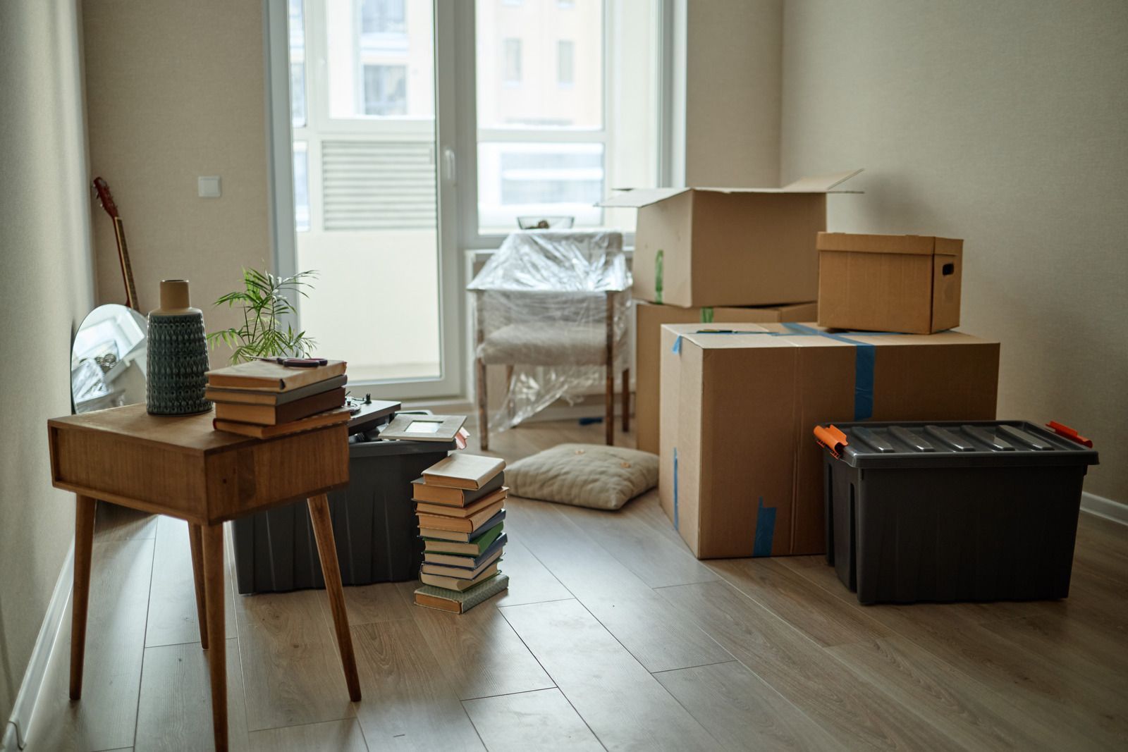 Cardboard moving boxes and packed belongings in a bright apartment near a window.
