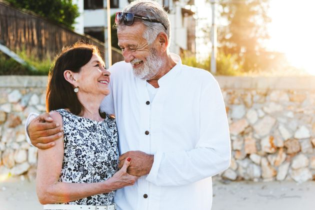 Smiling couple embracing outdoors by a stone wall in warm sunlight