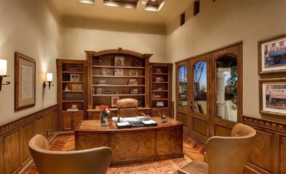 Luxurious home office with wood paneling, built-in bookshelves, a large desk, and two armchairs.