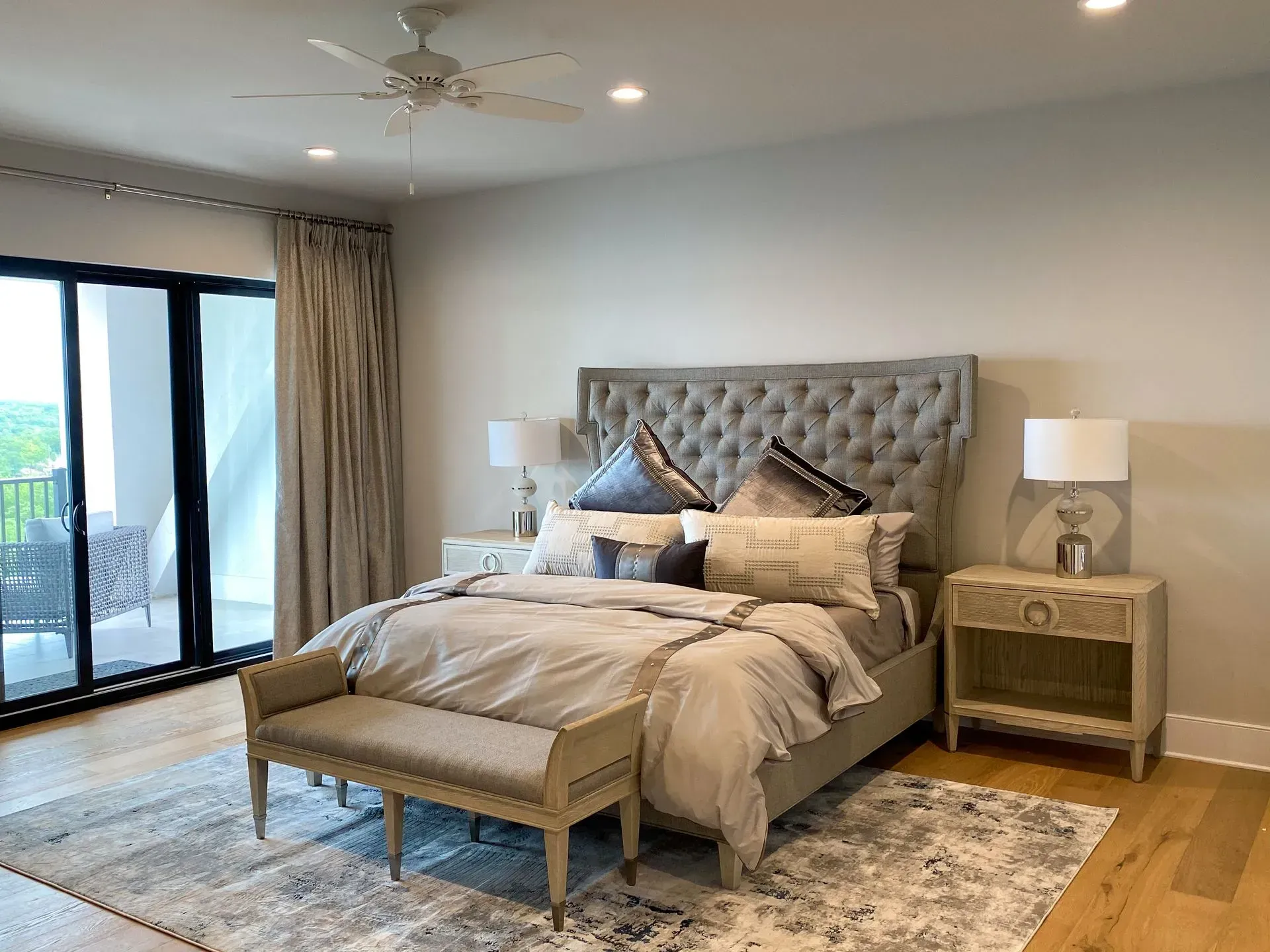 Bedroom with a gray tufted headboard, light bedding, and a bench. Features a rug, nightstands, and sliding door.