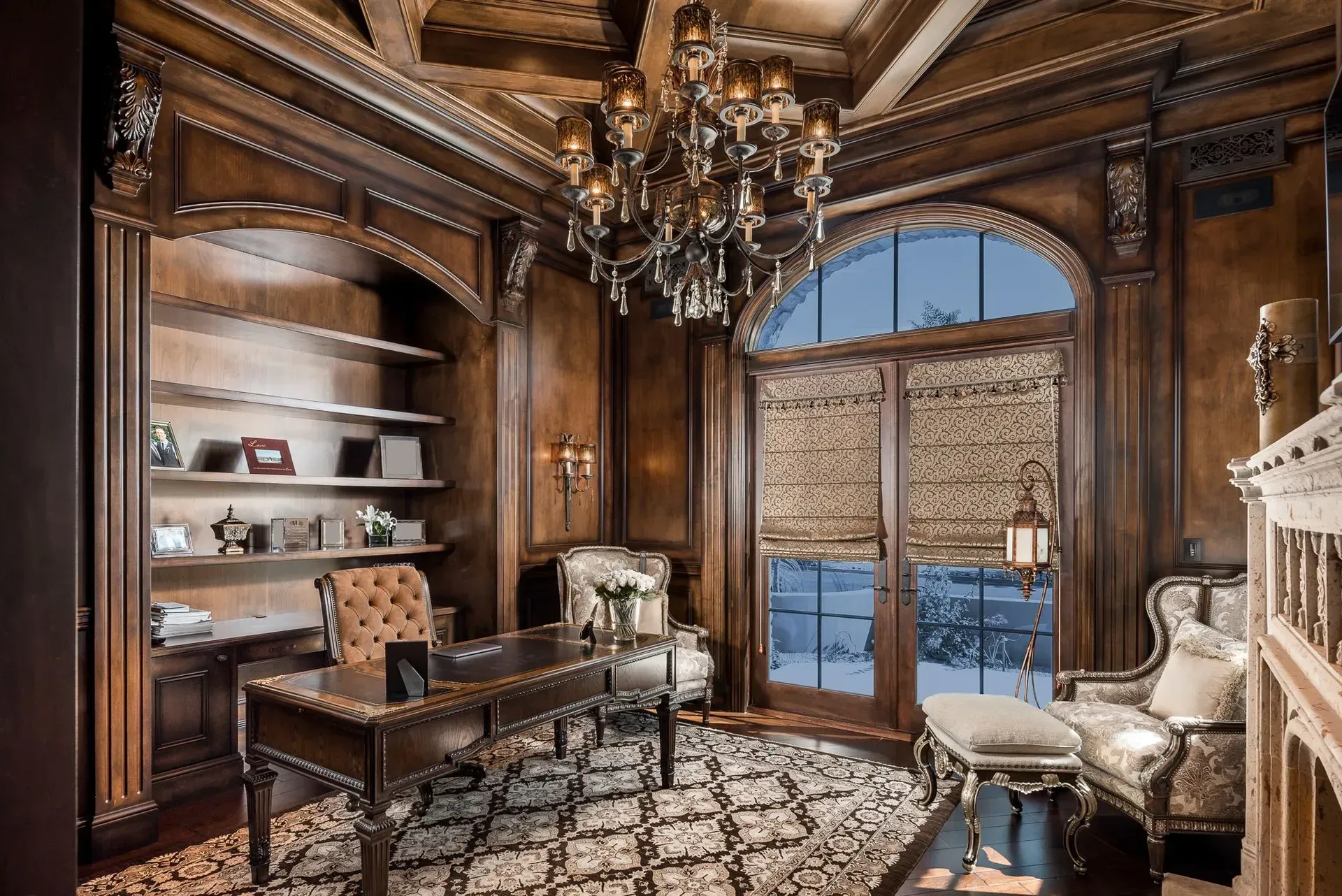 Elegant, wood-paneled study with ornate desk, bookshelves, and chandelier. Large window with snow view.
