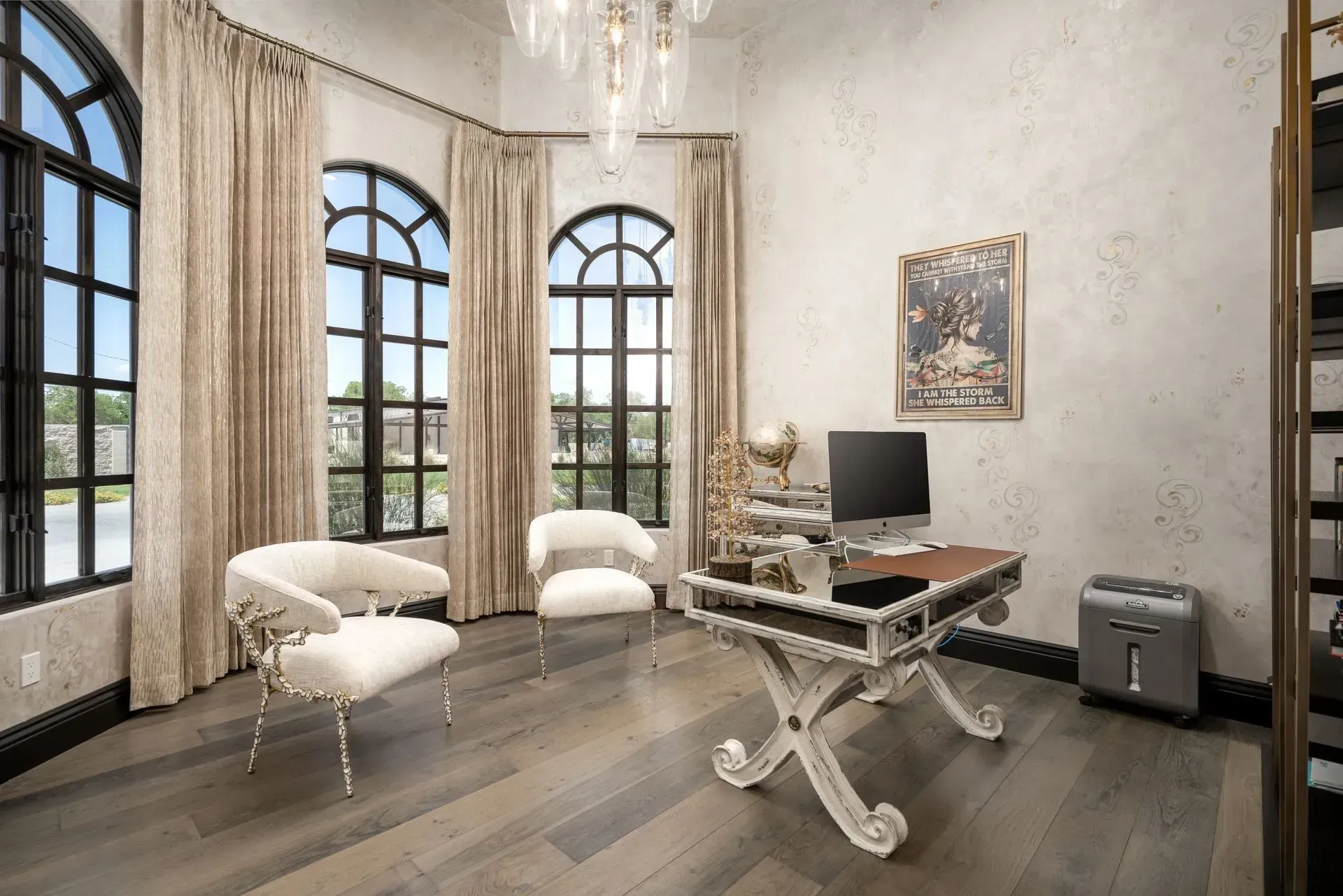 Elegant home office with arched windows, sheer curtains, a decorative desk, and two white chairs.