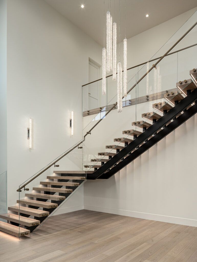 A modern staircase with a glass railing and a chandelier hanging from the ceiling.