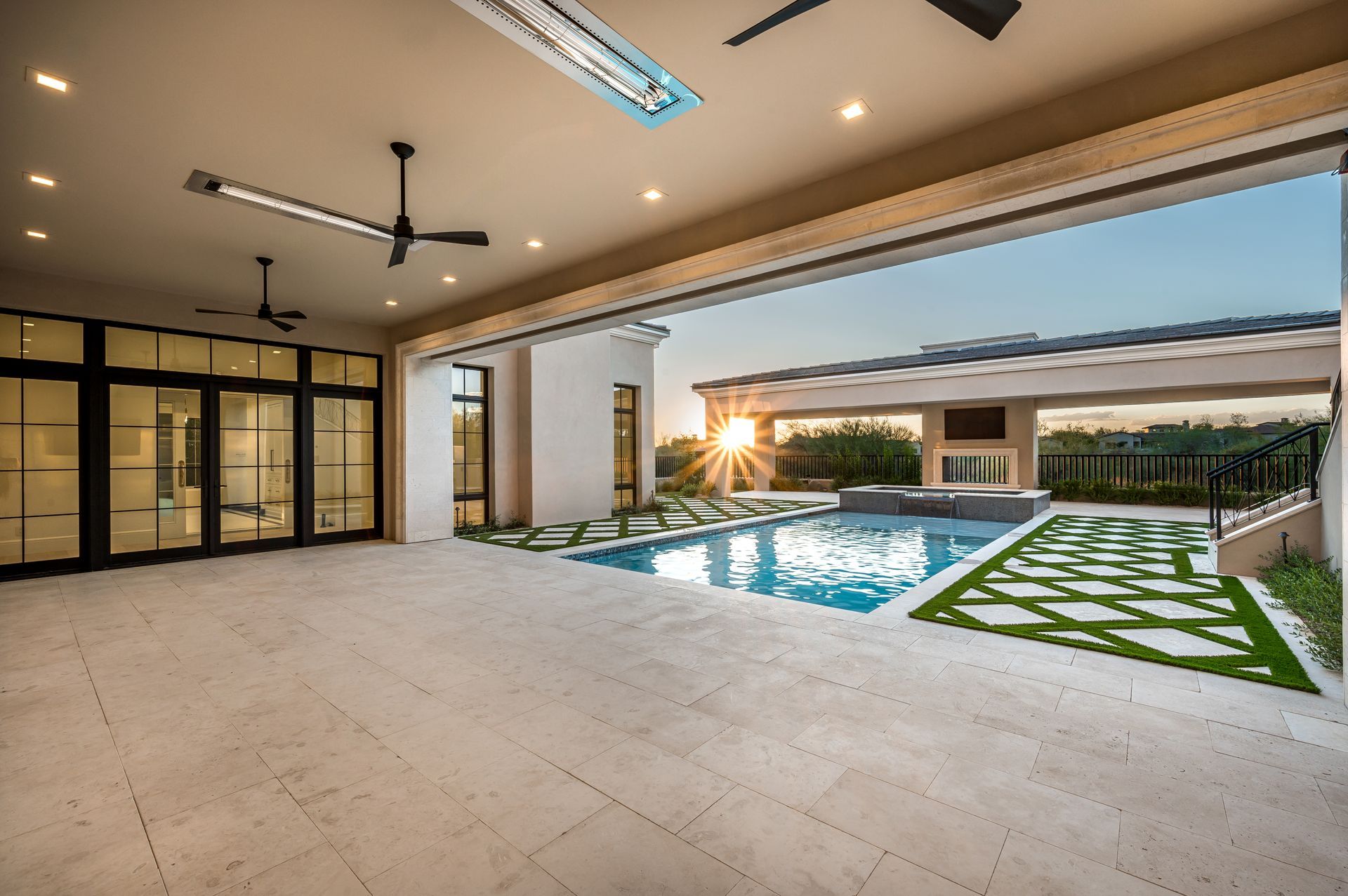 Modern luxury patio with pool, open glass doors, and sunset view