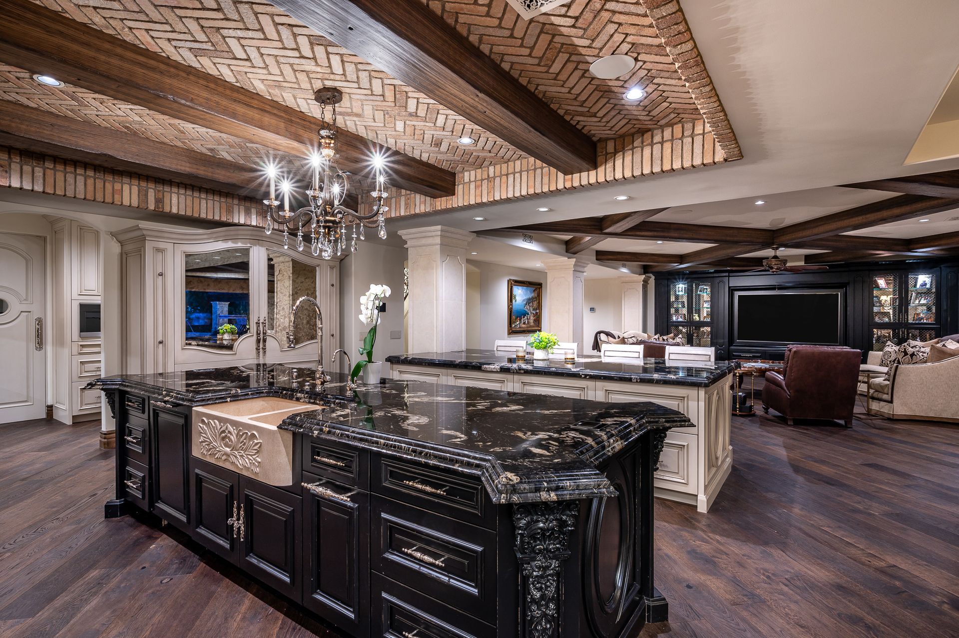 Luxurious kitchen with black granite island, chandelier, wooden beams, and a view of a living area.