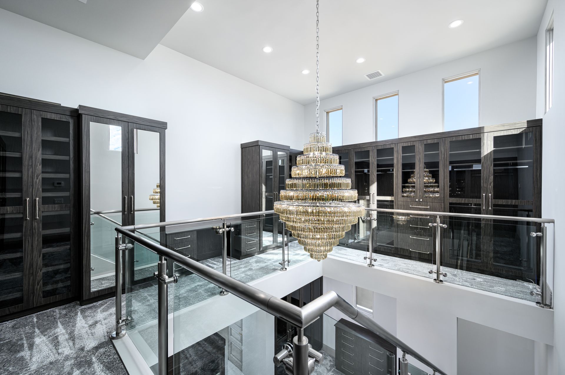 Luxury walk-in closet with dark wood cabinets, a large chandelier, and a glass-railed balcony.