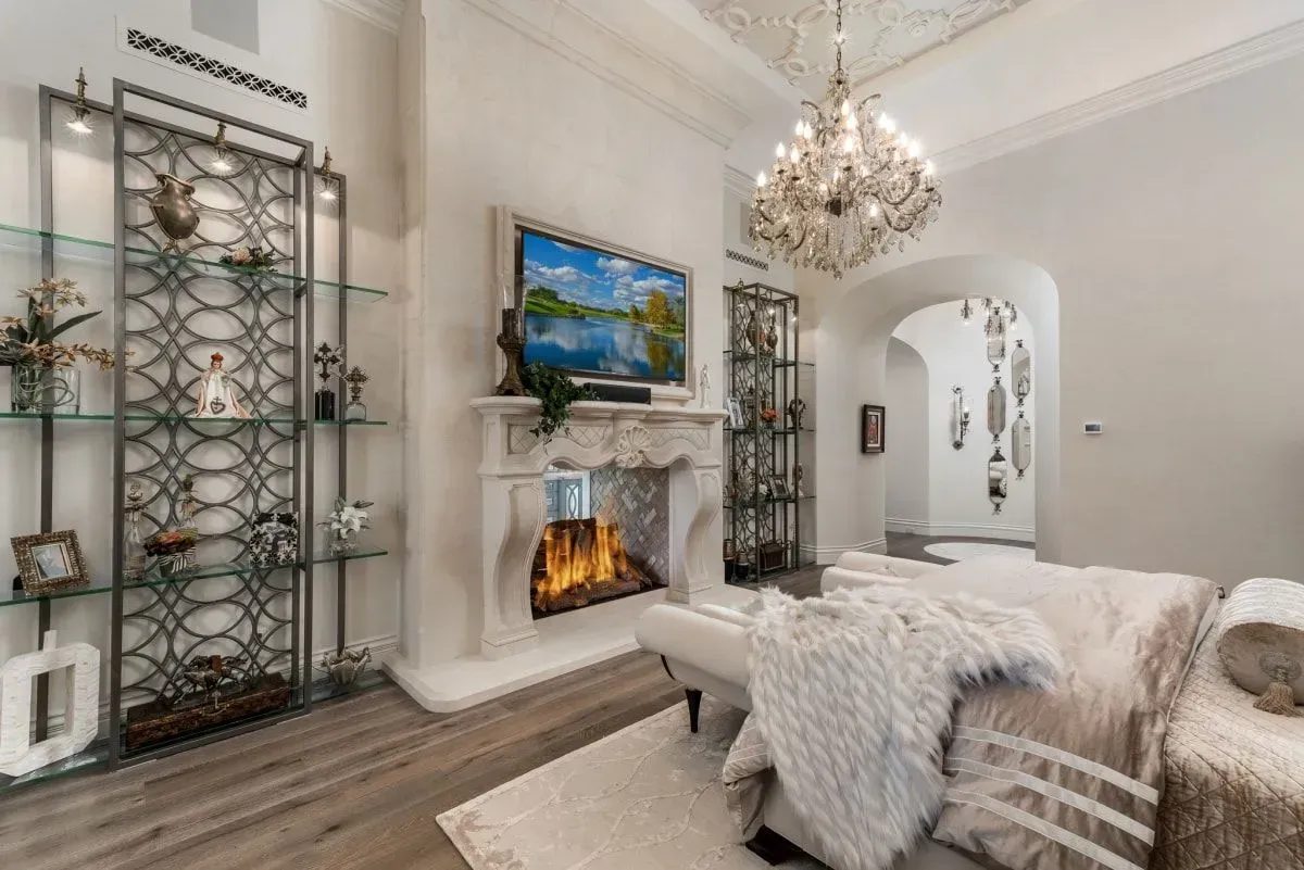 Elegant living room with fireplace, chandelier, and display shelves, all in shades of white and gray.