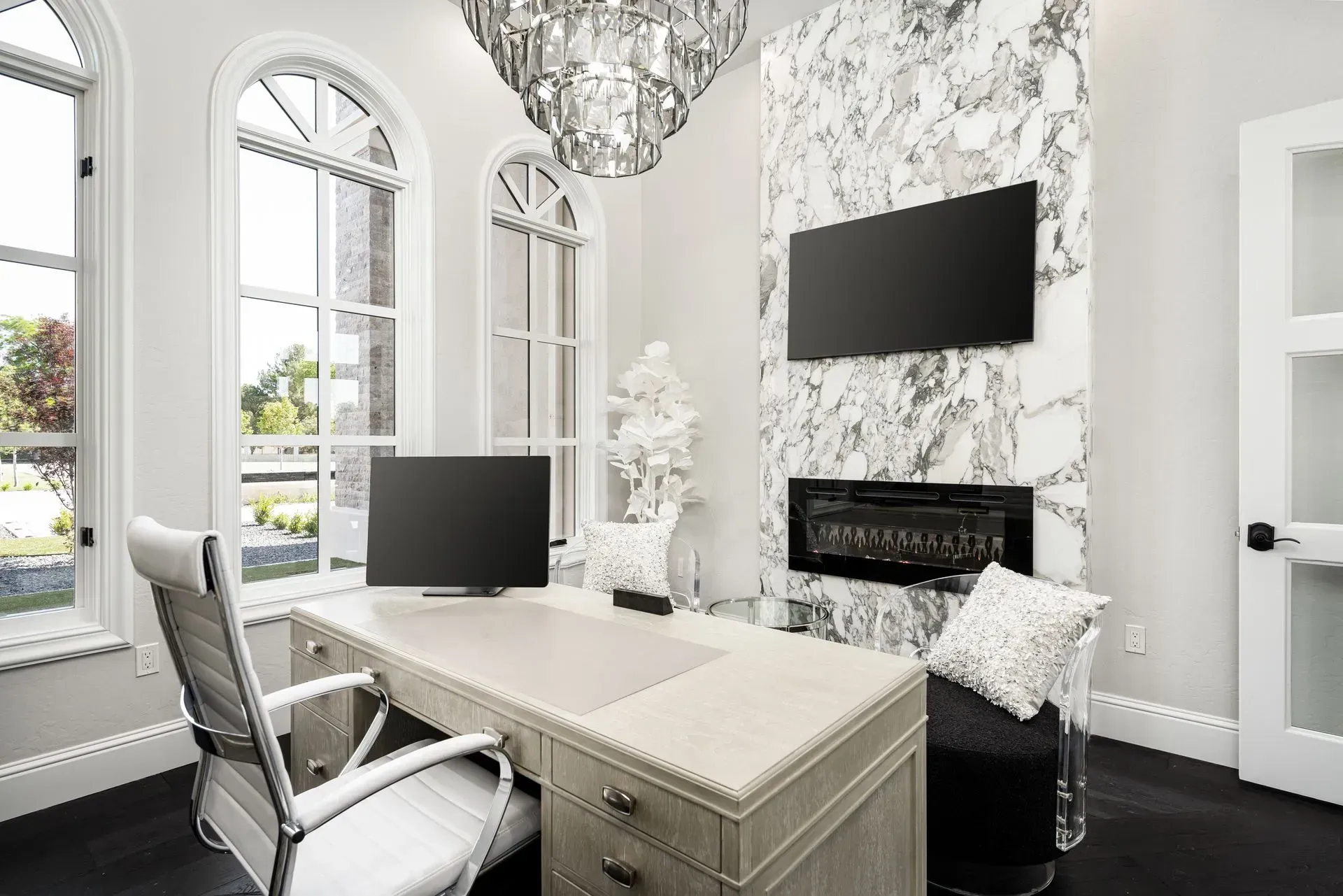 Elegant home office with desk, chair, marble fireplace, and large windows.