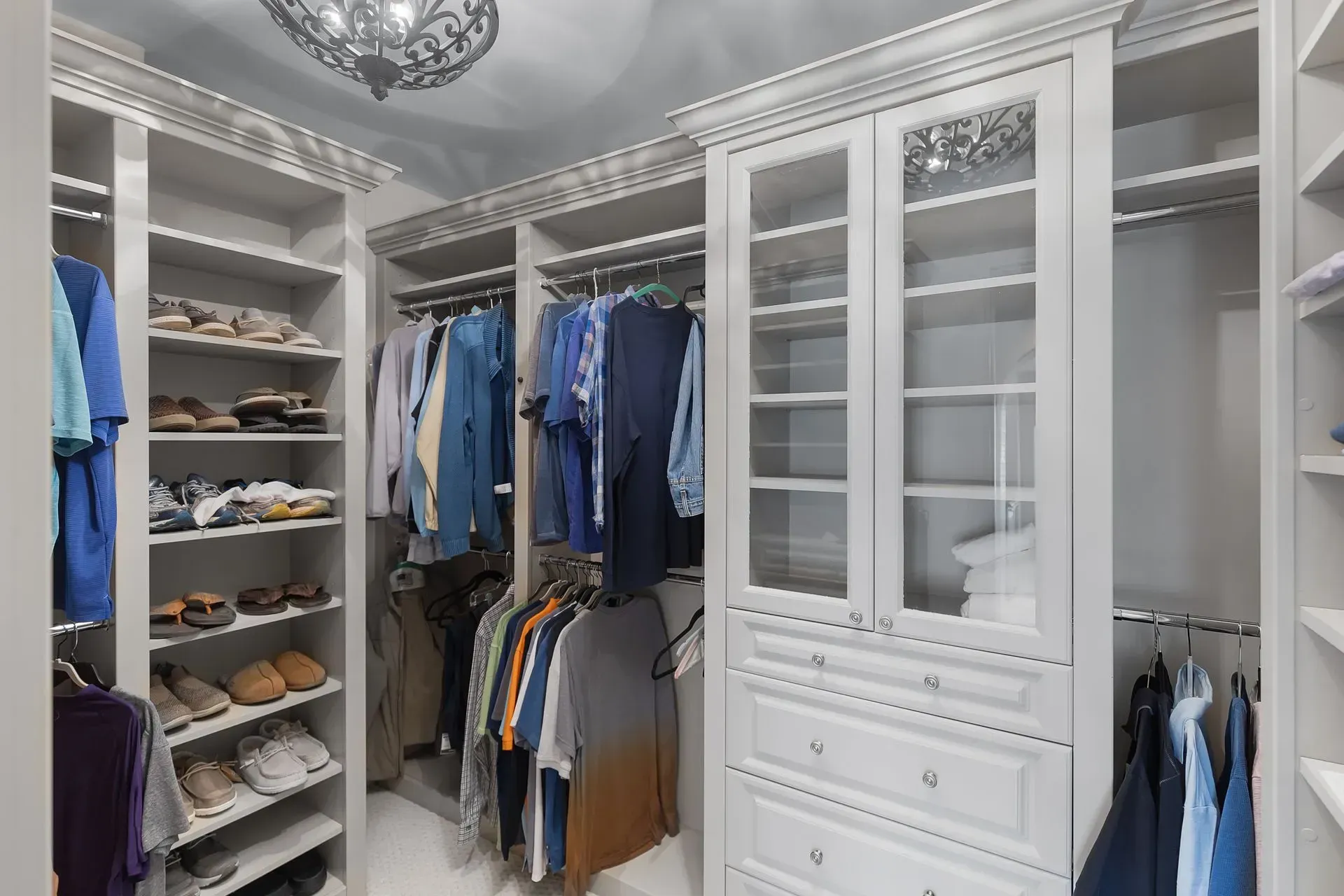 Walk-in closet with gray shelves and cabinets holding shoes and hanging clothes.
