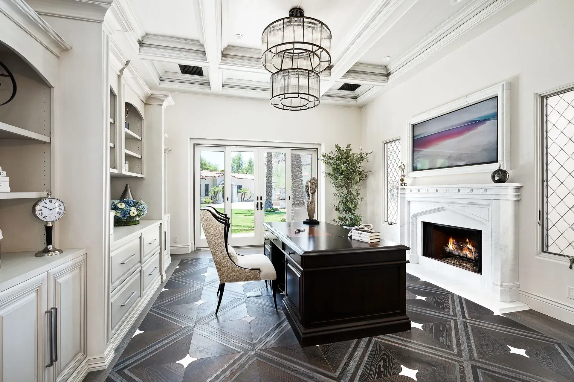 Luxurious home office with dark desk, fireplace, and ornate ceiling. Opens to a patio.