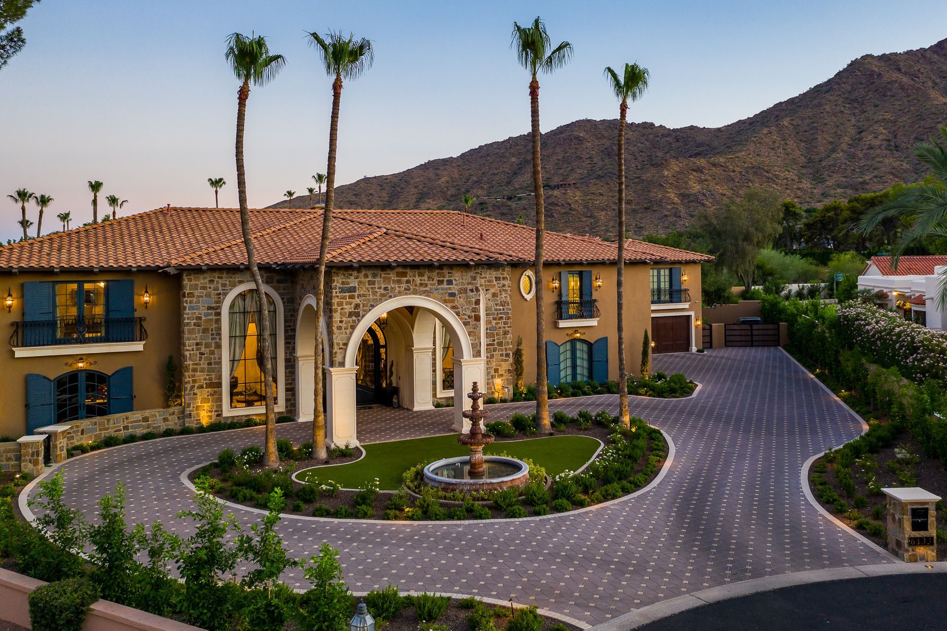 Mansion with arched entry, palm trees, and mountain backdrop at dusk