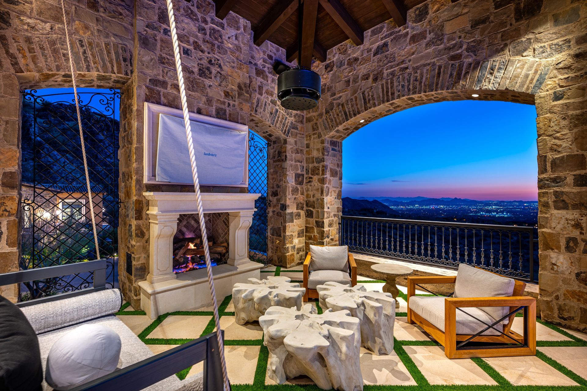Luxury stone patio lounge with white furniture, fireplace, and Arizona sunset view