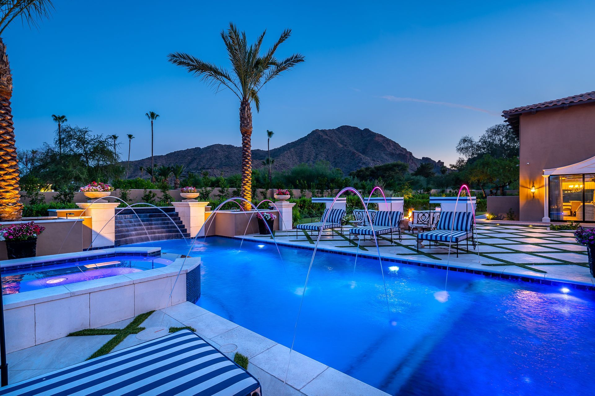 Luxury pool at dusk with lounge chairs, palm trees, and a mountain backdrop