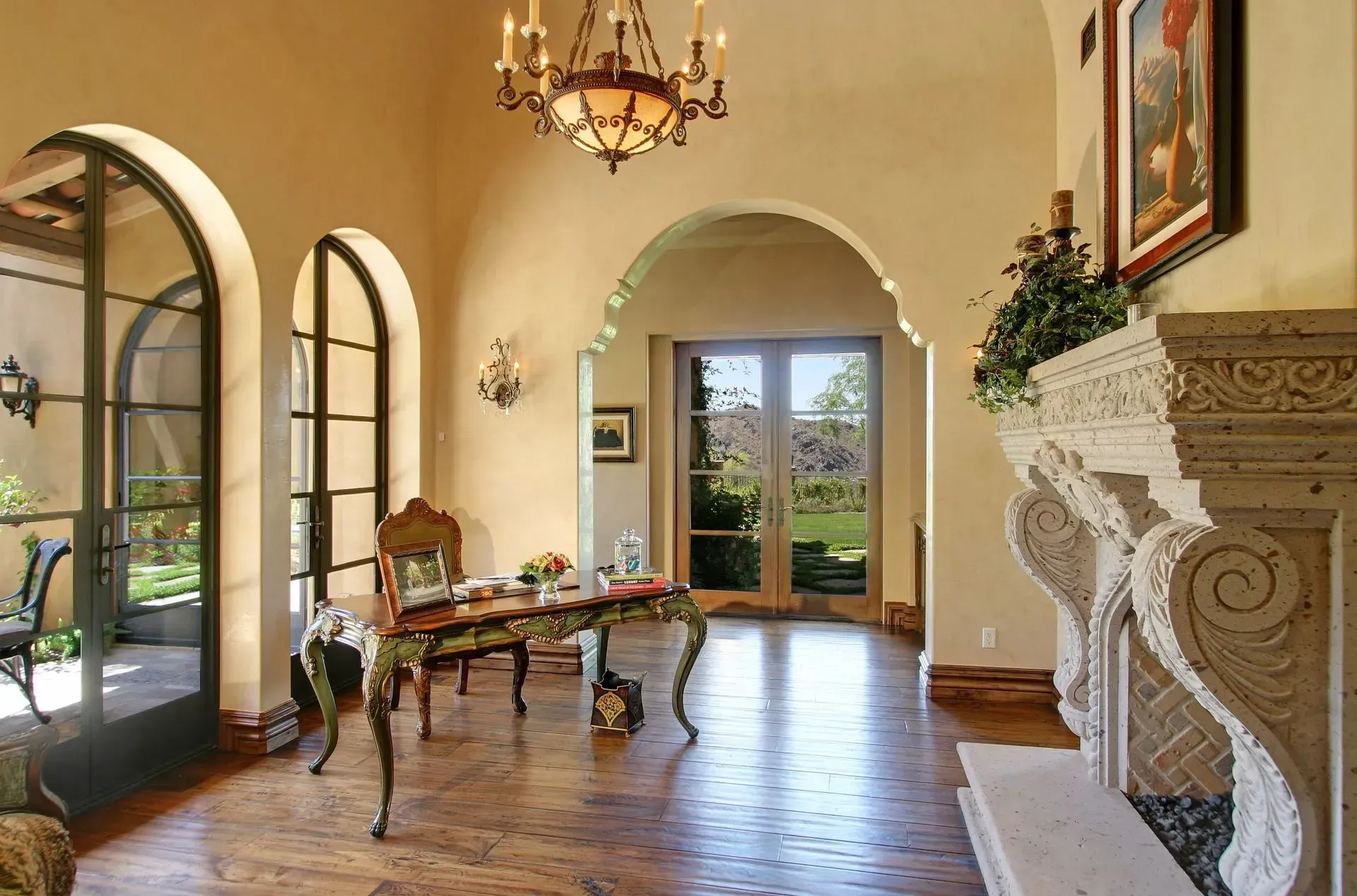 Elegant interior with arched doorways, ornate fireplace, desk, and outdoor view.