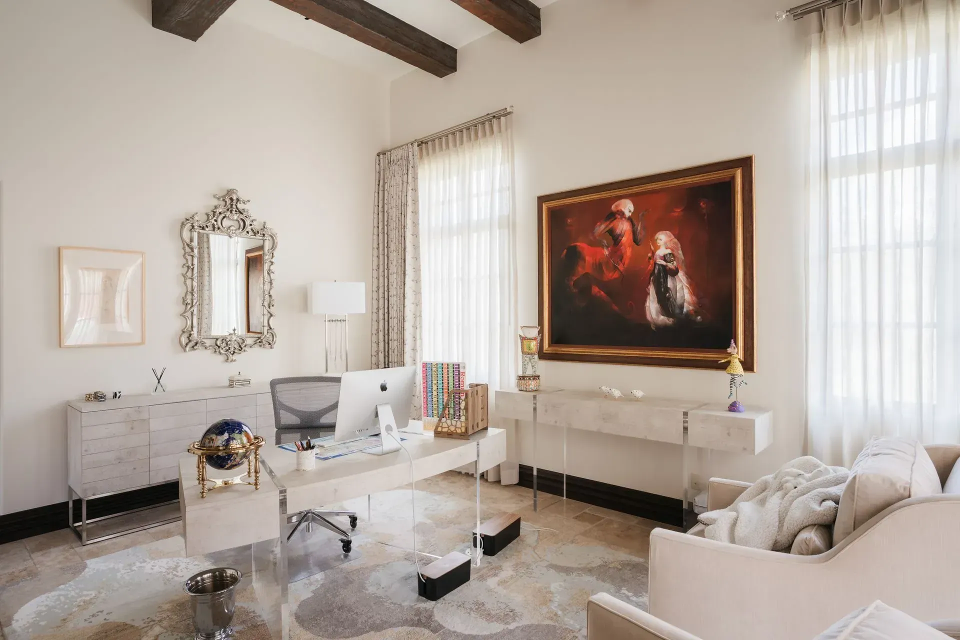 Elegant home office: desk, artwork, mirror, white walls, and sheer curtains.