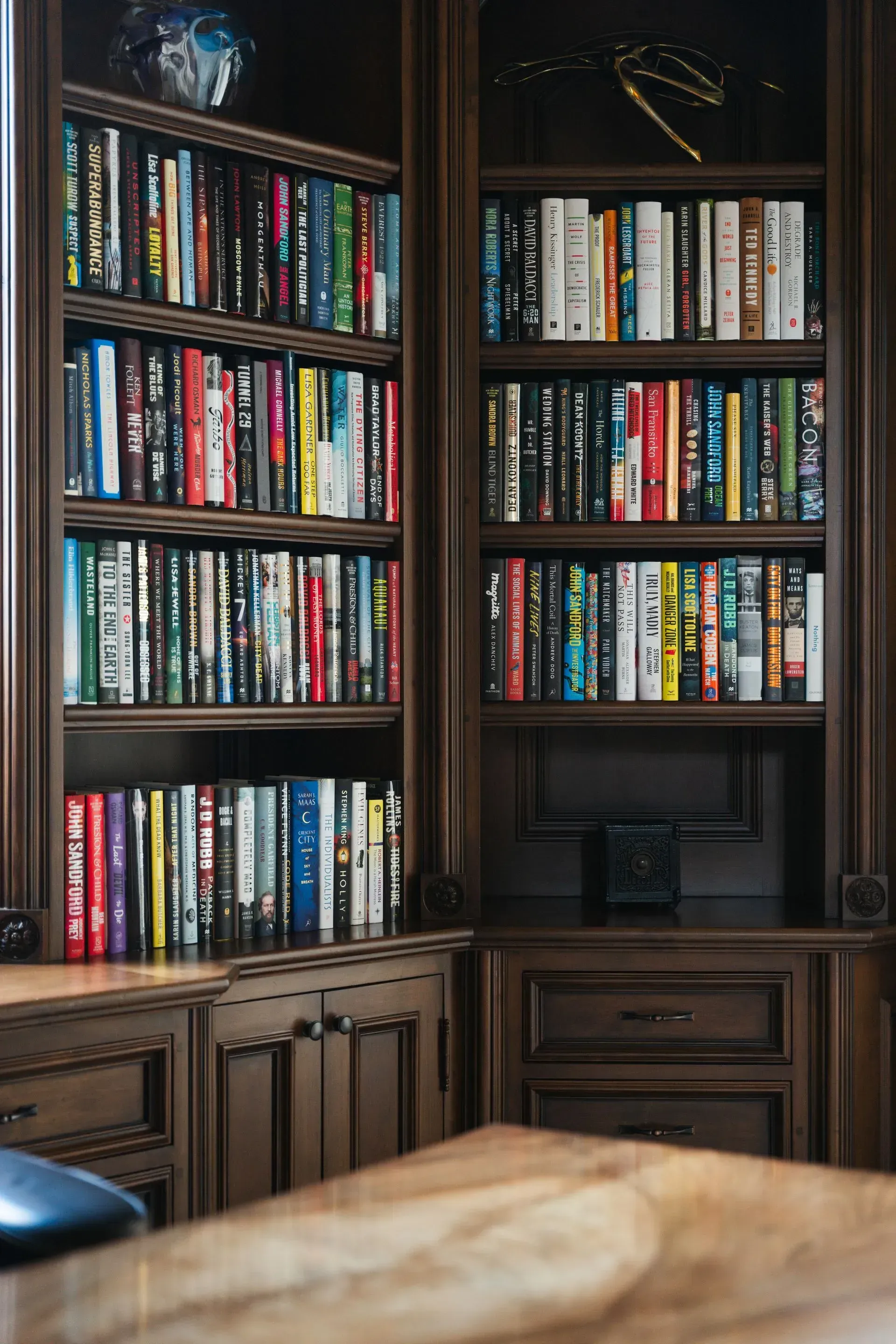 Wooden bookshelves filled with books in a home library. Brown cabinets, varied book spines.