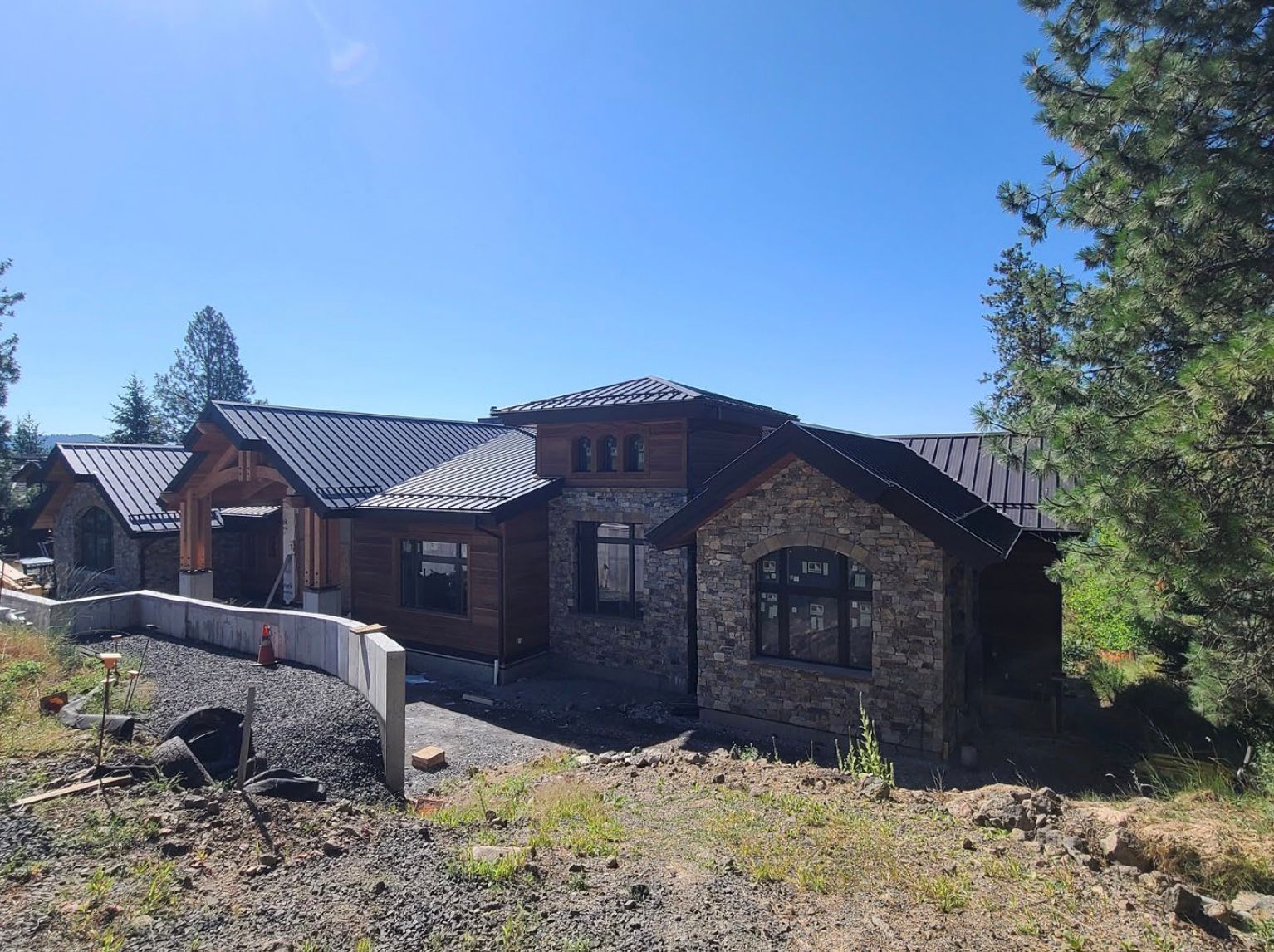 New house under construction with stone and wood exterior, dark roof, blue sky.